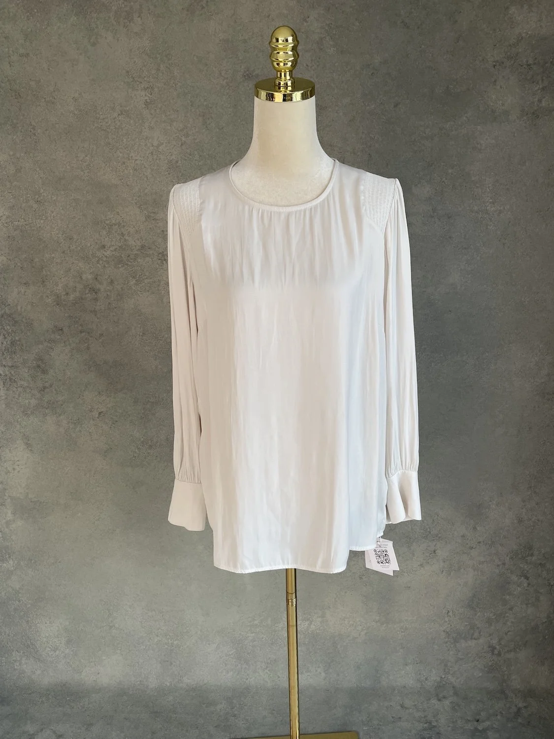 Gigue silky beige blouse featuring a round neckline, subtle shoulder gathering, and long sleeves, displayed on a mannequin against a neutral textured backdrop.