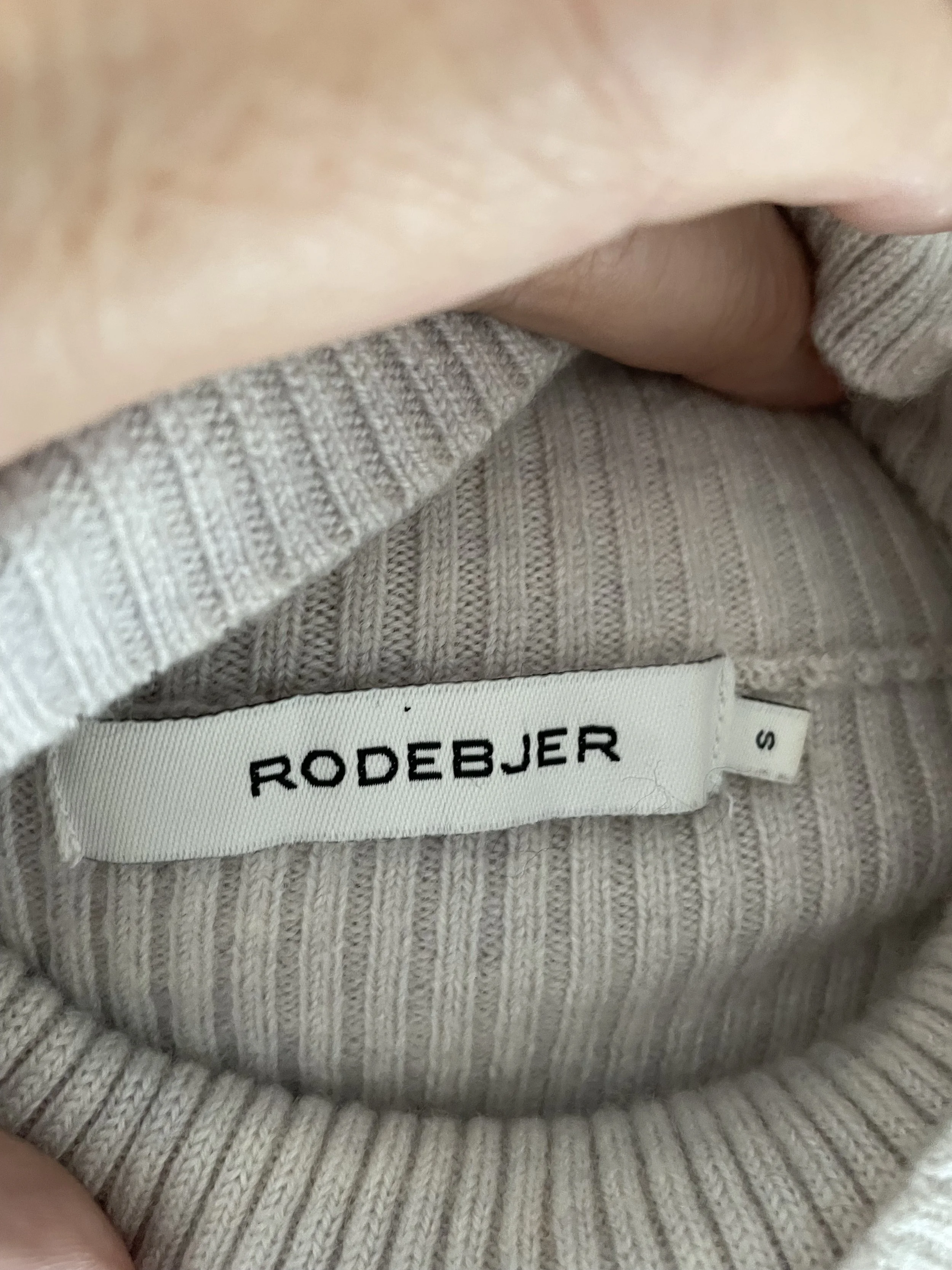 Detailed close-up of the Rodebjer brand label inside the neckline of the grey ribbed jumper.