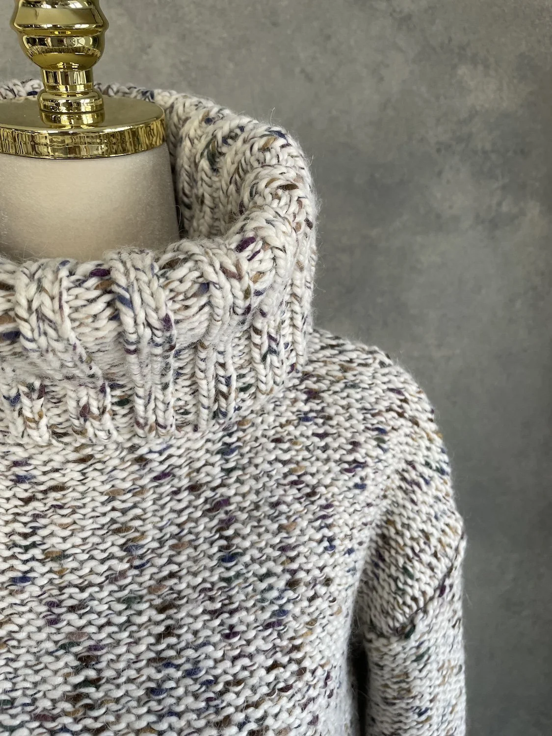 Close-up of the thick ribbed turtleneck collar on the Essentiel Antwerp speckled knit sweater, highlighting the multicolored yarn flecks.