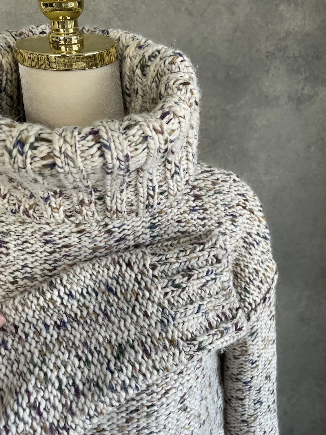Close-up showing the heavy knit texture and folded cuff of the Essentiel Antwerp speckled sweater.