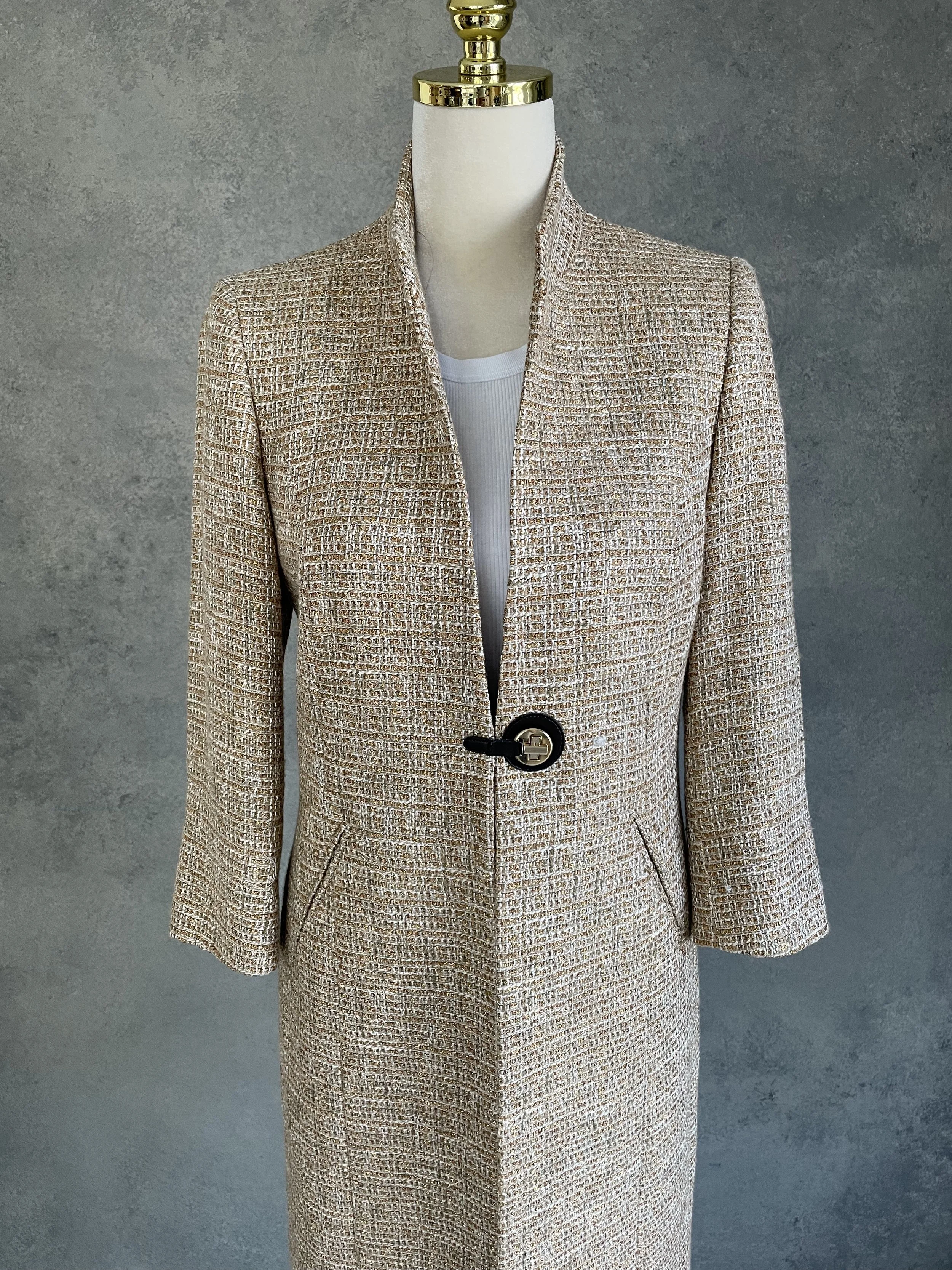 Detailed close-up of the metallic gold tweed fabric texture and black toggle fastener.