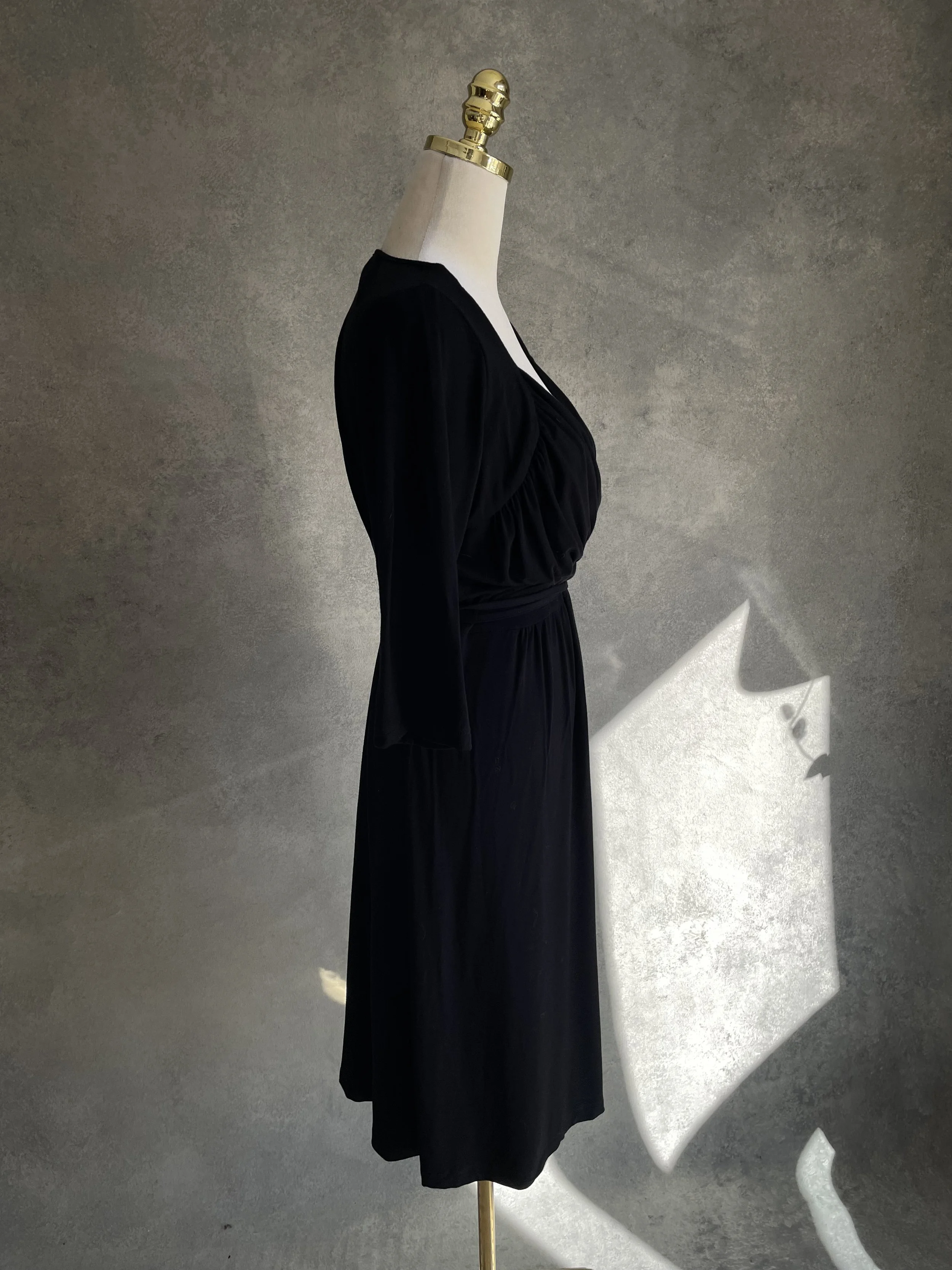 Side profile view of the Scapa black jersey wrap dress on a mannequin, showing the fit and silhouette."