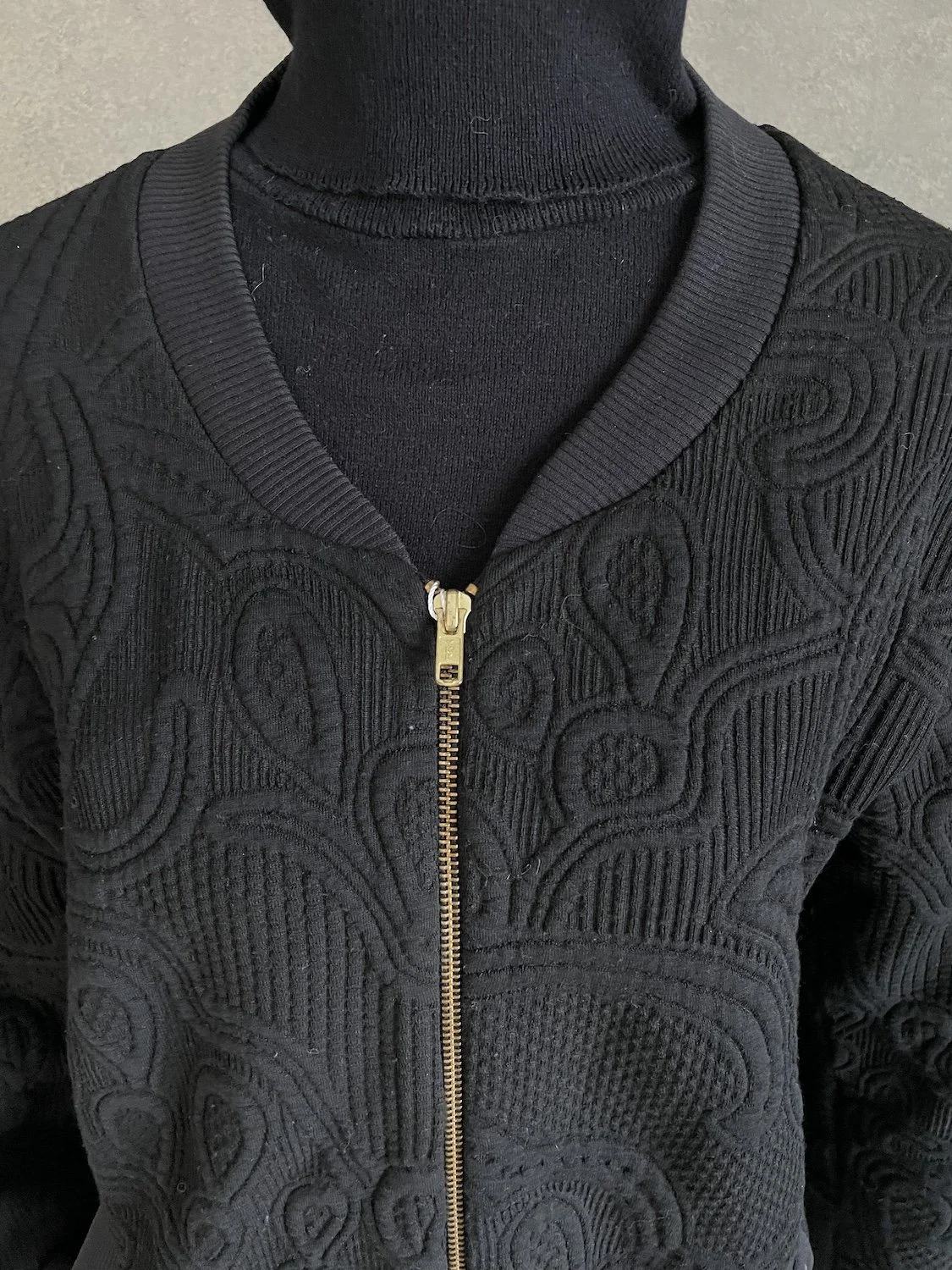 Close-up of the center front gold zipper and high-neck ribbed collar layering.