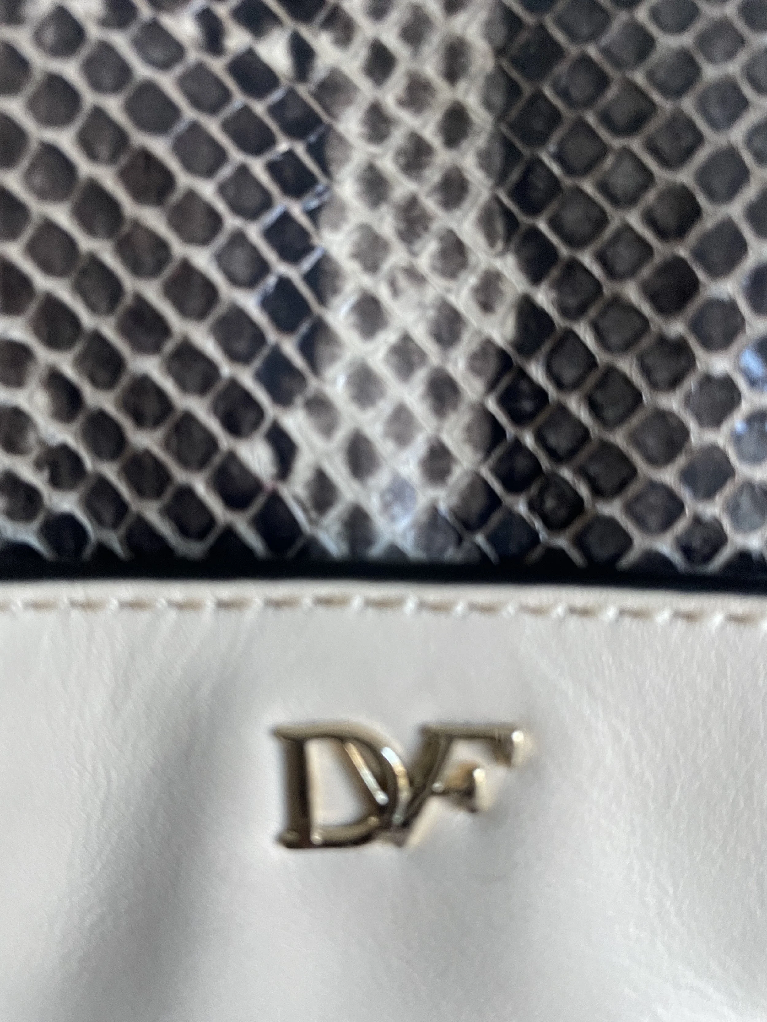 Close-up detail of the embossed "DVF" logo on the cream leather body of the bag.