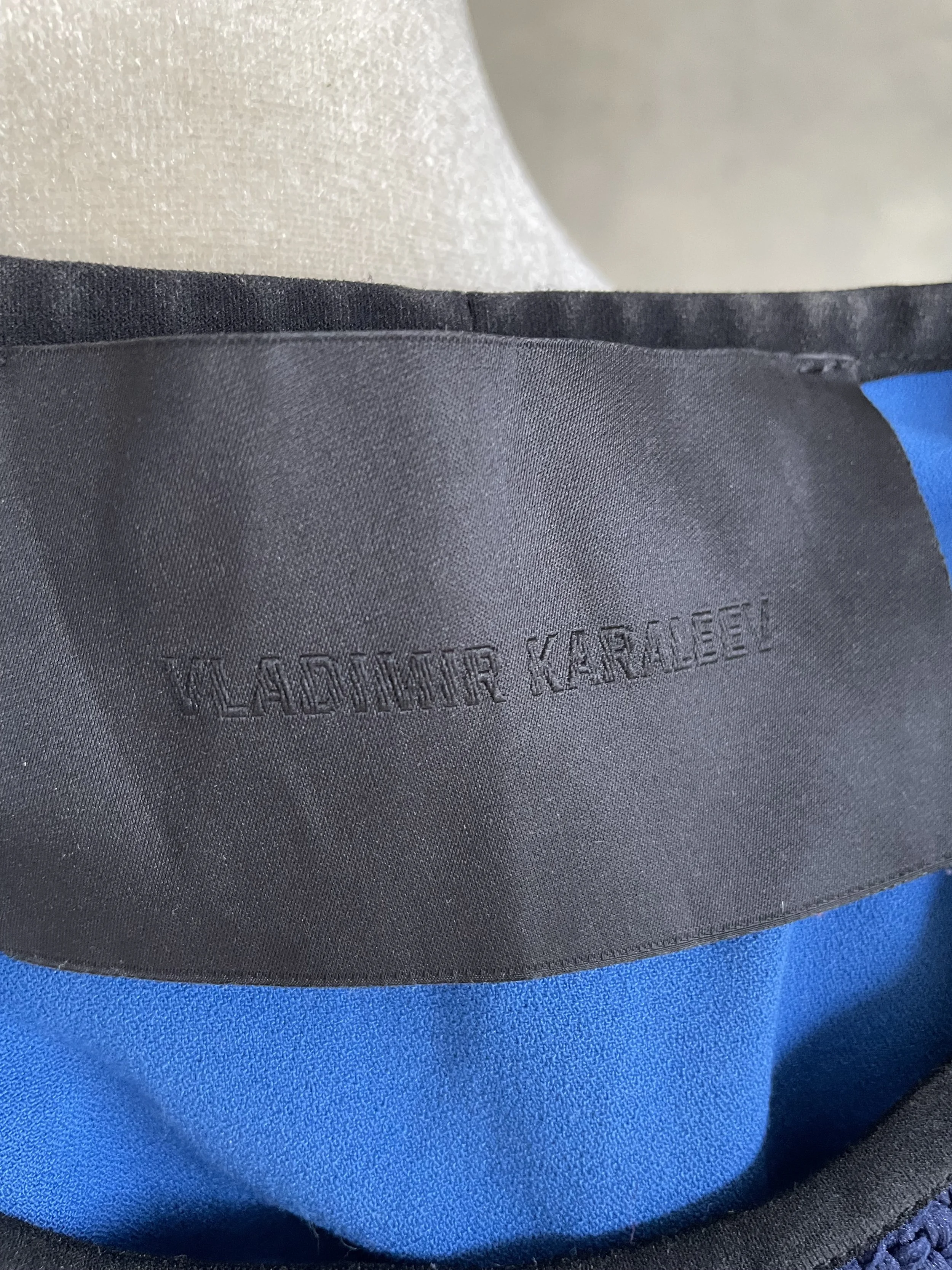 Close-up of the black garment tag with the brand name "Vladimir Karaleev" embroidered in black.