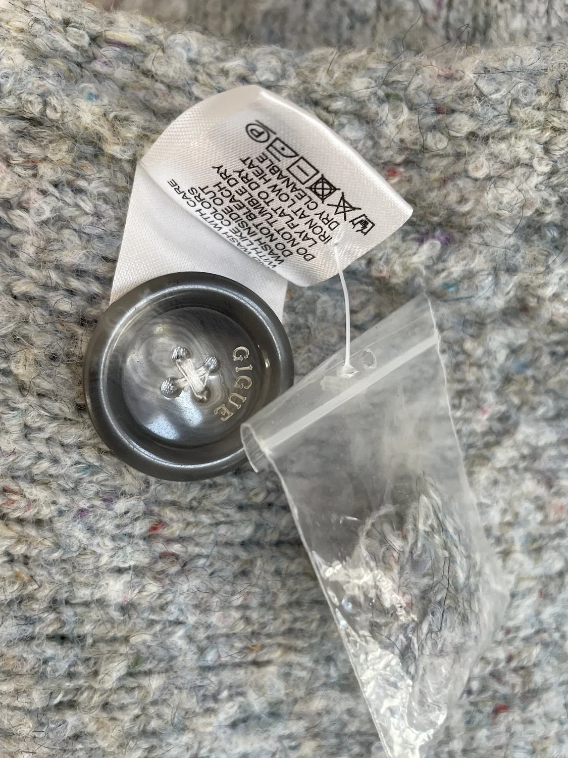 Close-up of the care label and attached small plastic pouch containing an extra replacement button.