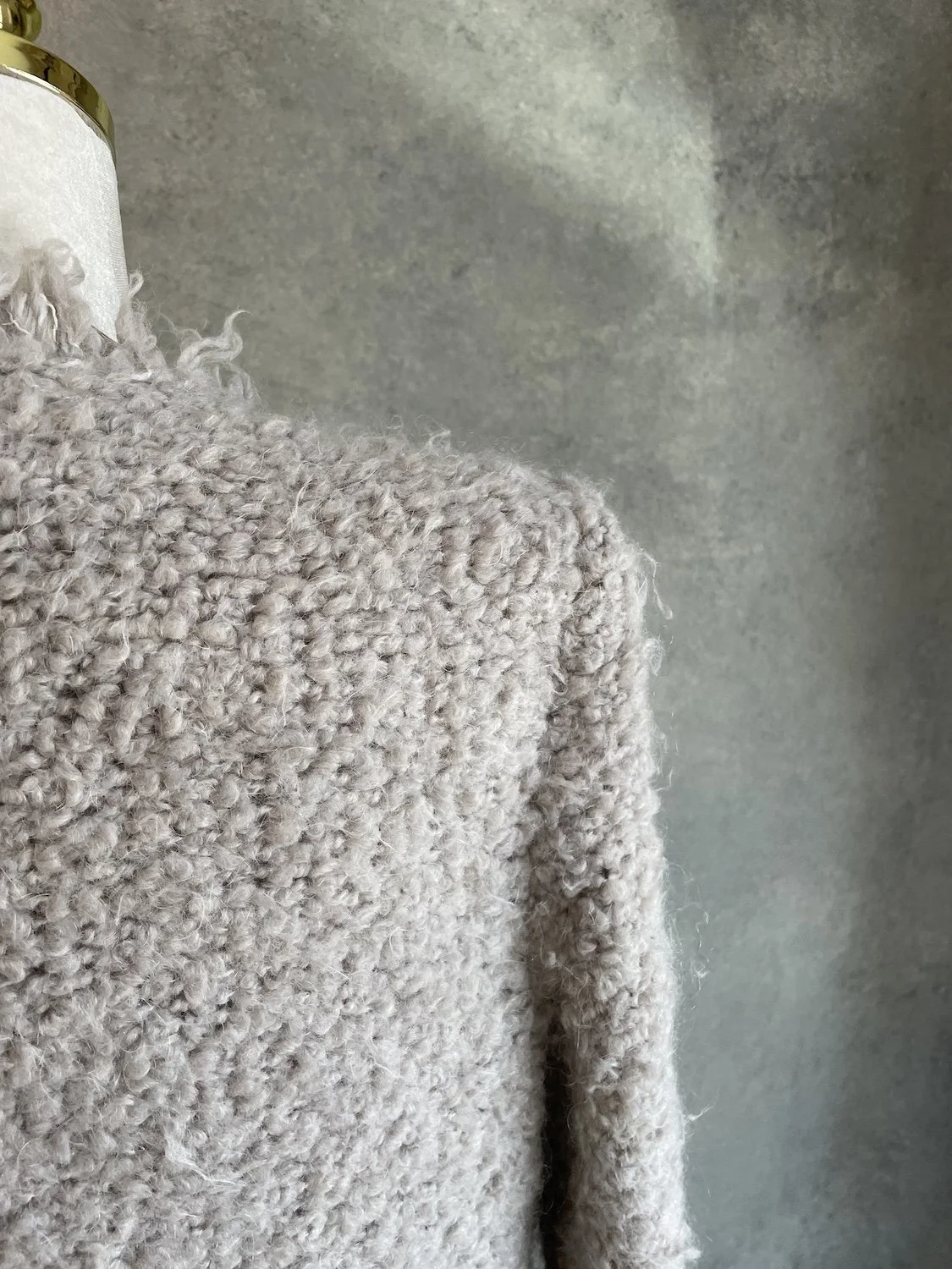 Macro close-up of the shoulder seam and textured fabric weave in neutral beige and taupe tones.