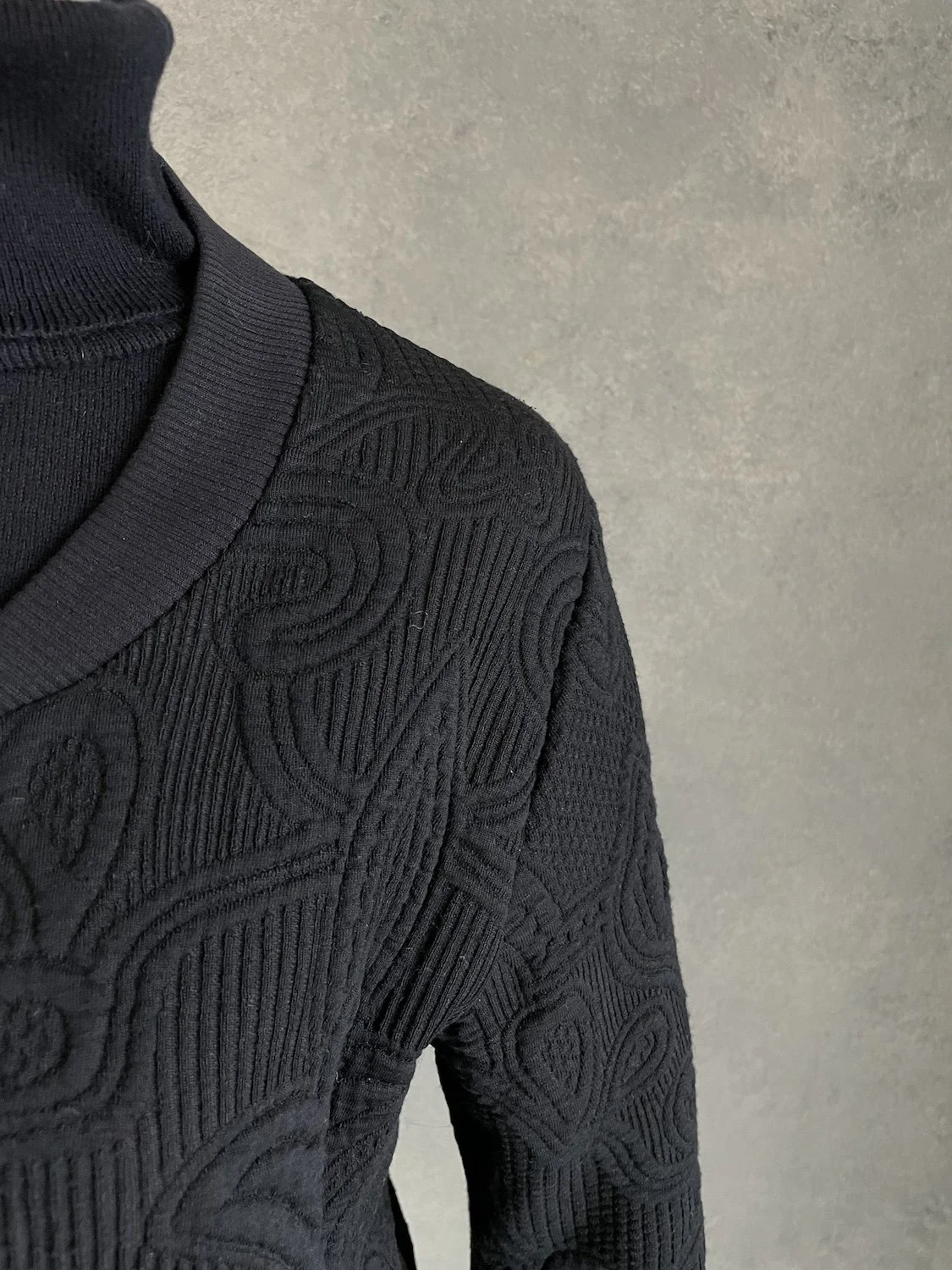 Close-up of the right shoulder and structured collar ribbing with floral relief texture.