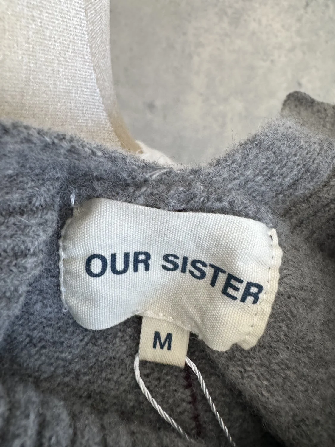 Close-up of the sewn-in "OUR SISTER" neck label and the "M" size tag.