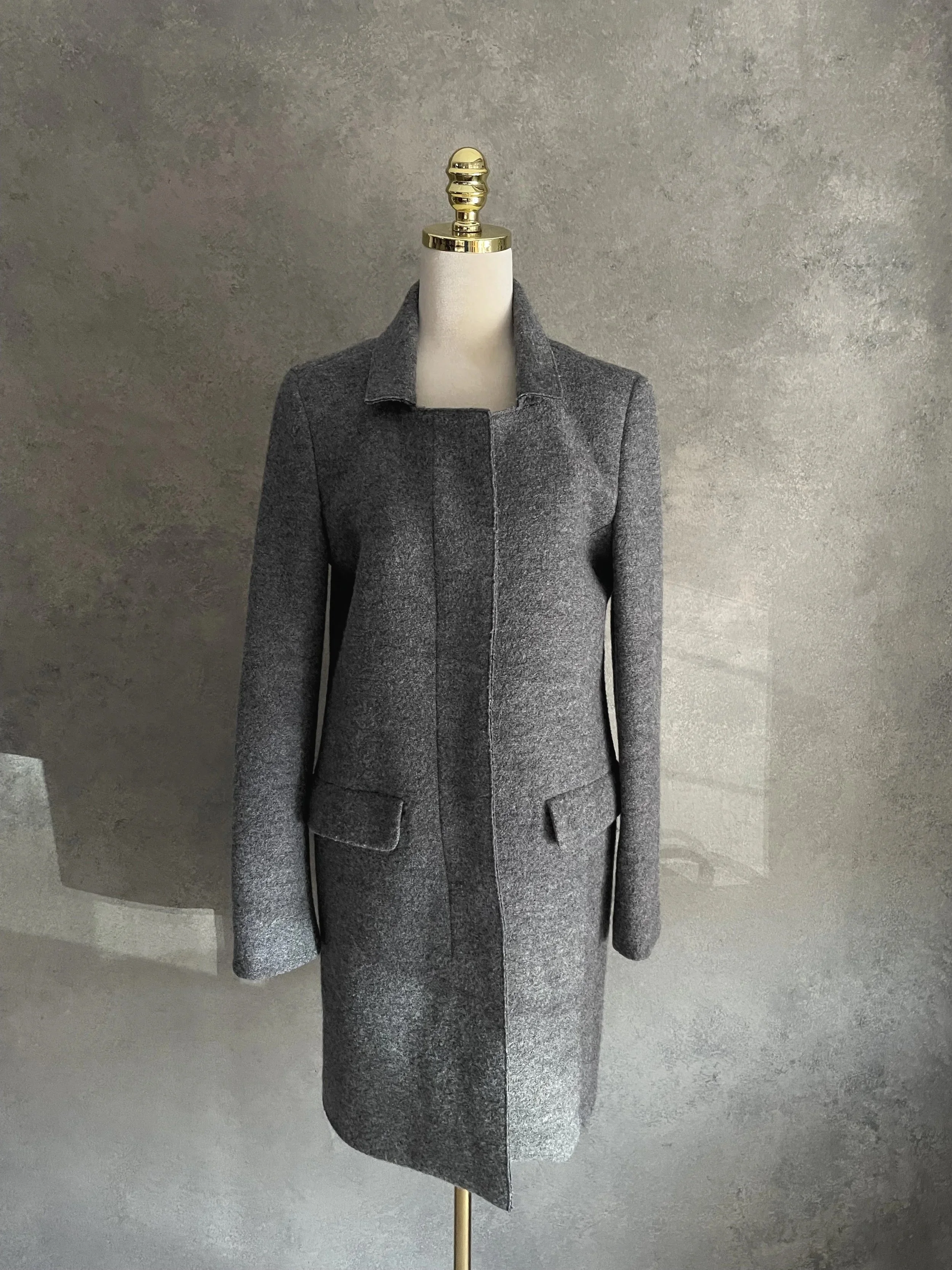 Front view of the grey wool coat by Closed on a mannequin with the concealed button placket closed, highlighting the seamless tailored design