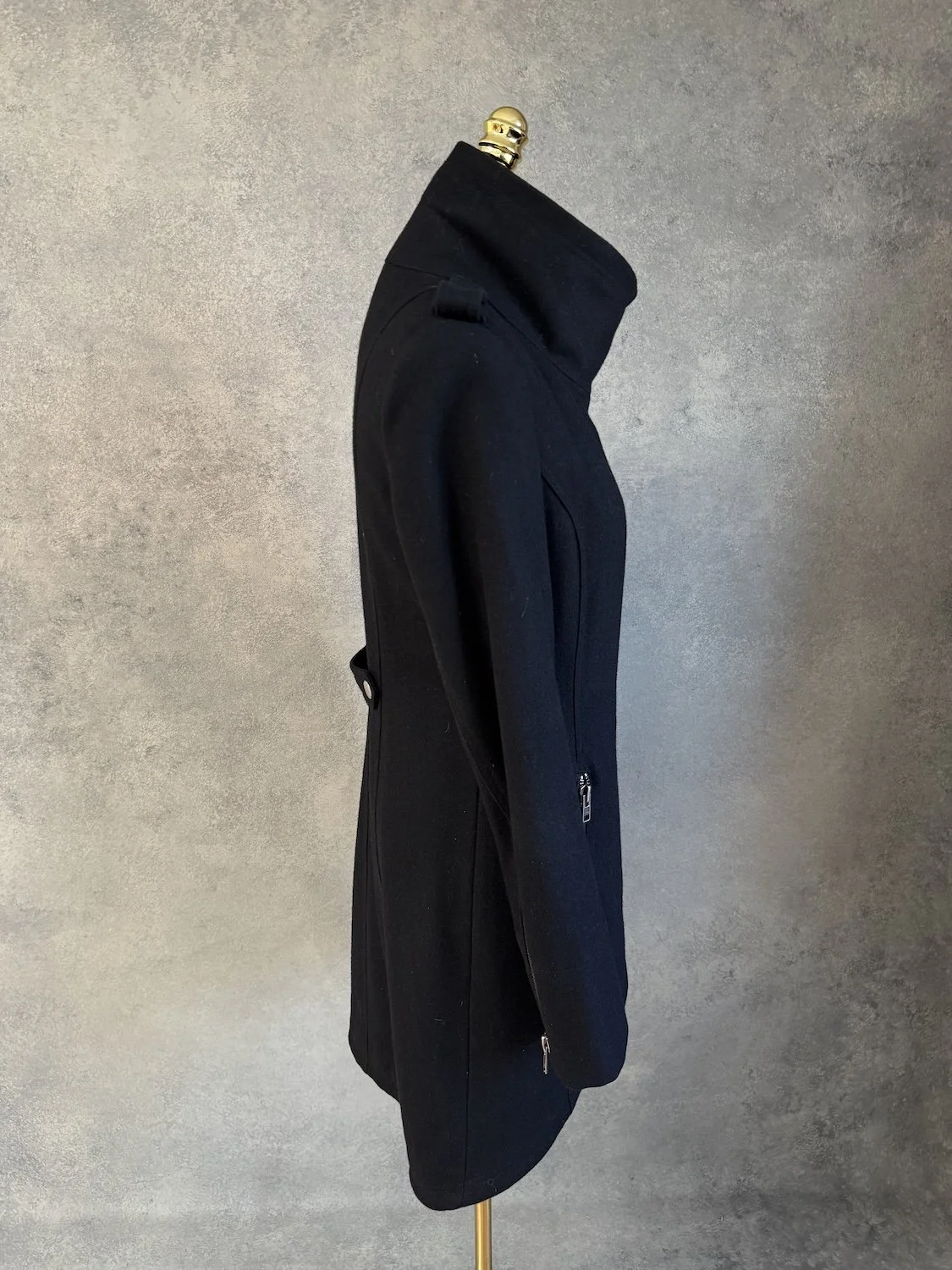 Side profile view of the black coat on the mannequin, showing the tailored fit.