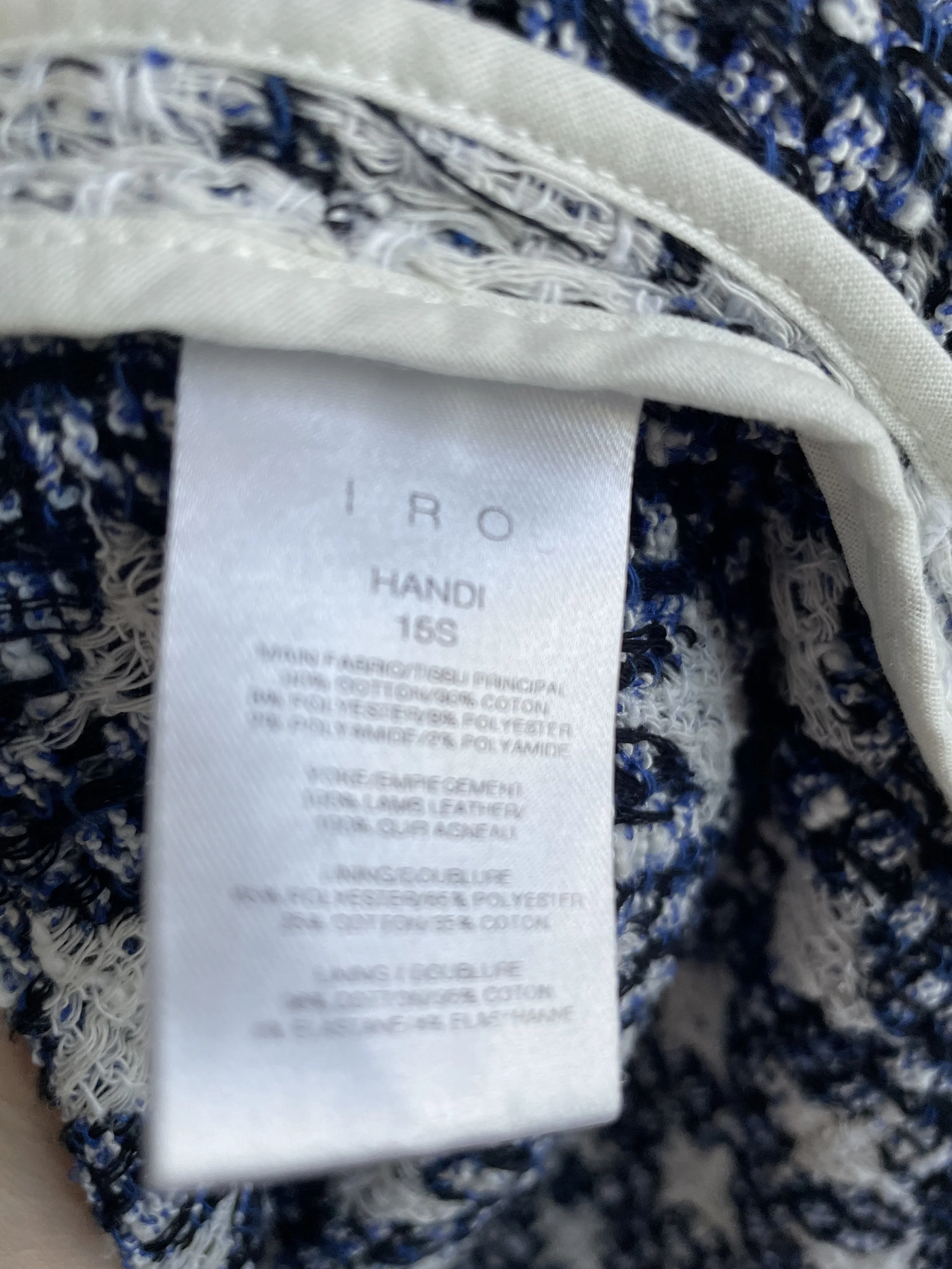 Close-up of the interior care and composition label detailing the 'HANDI' style name, 16S season, cotton-polyester blend, and lamb leather trim.