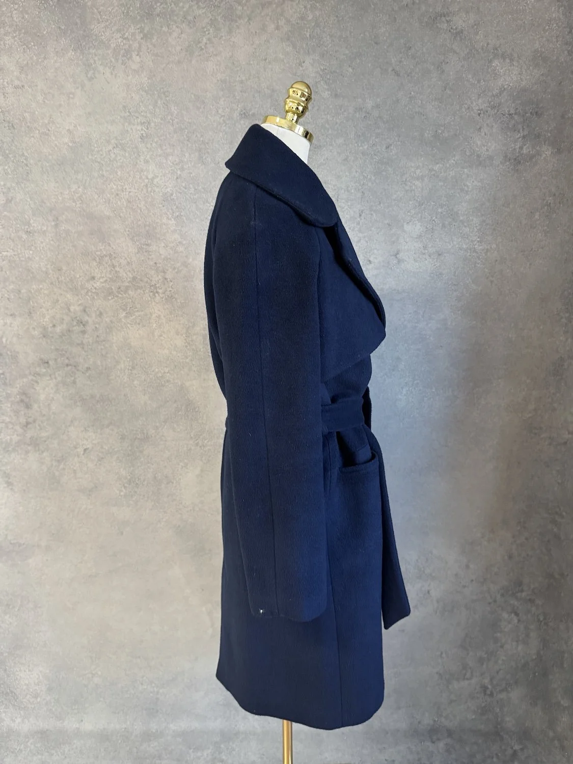 Side profile view of the navy blue wrap coat on the mannequin, showing the structured shoulder and belted waist.