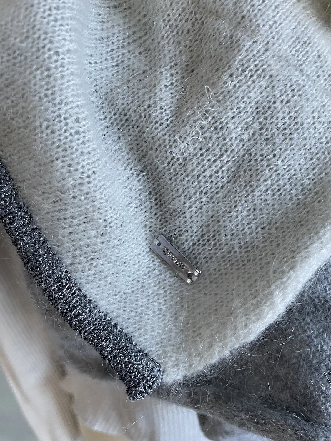 Close-up of the metal Gustav brand plaque attached to the edge of the knit fabric.