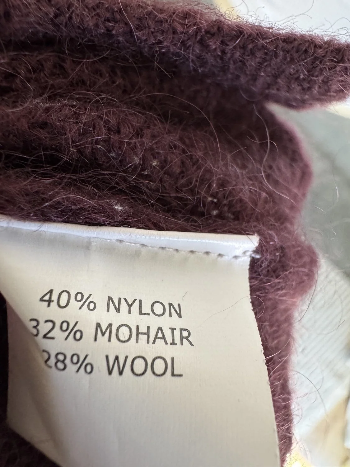 Nahaufnahme des Materialetiketts: "40% NYLON, 32% MOHAIR, 28% WOOL"