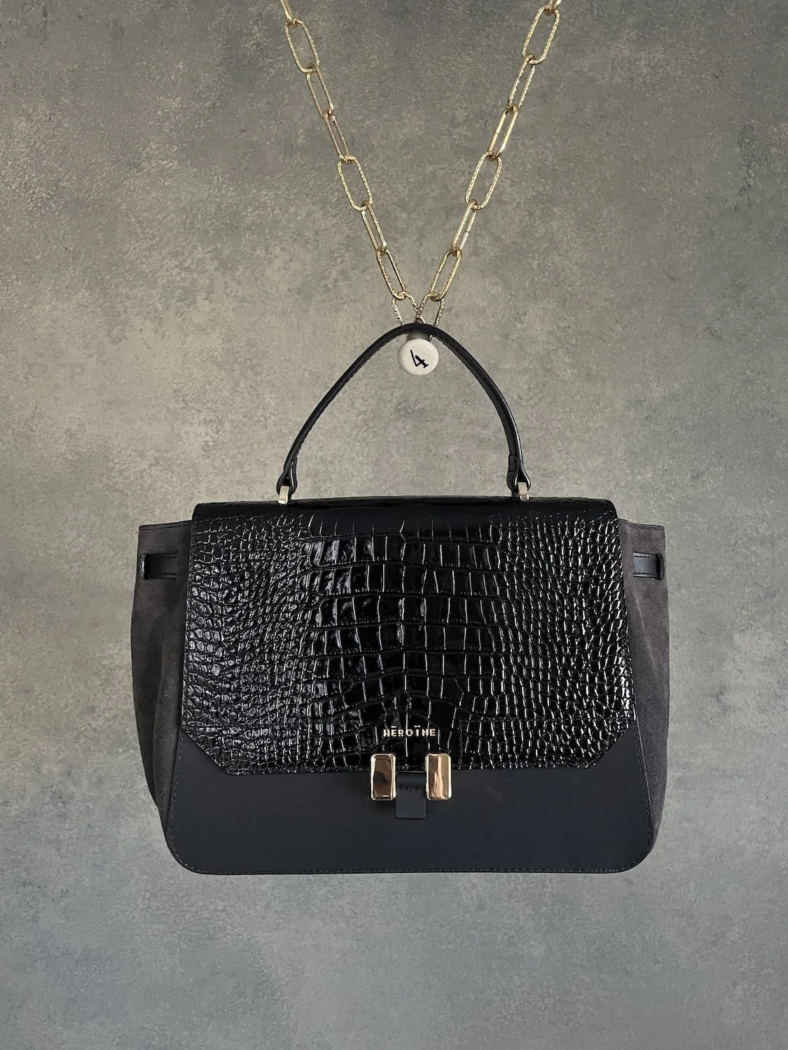 Maison Héroïne schwarze Leder-Handtasche mit Krokodil-Prägung und Tragegriff vor grauem Hintergrund