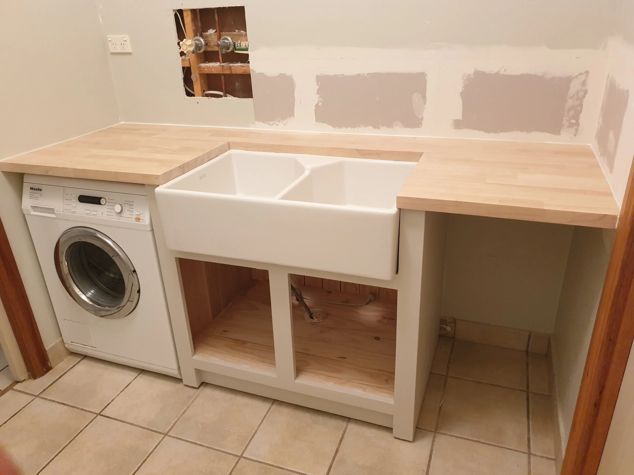 Laundry with plasterboard repairs and wooden bench tops.