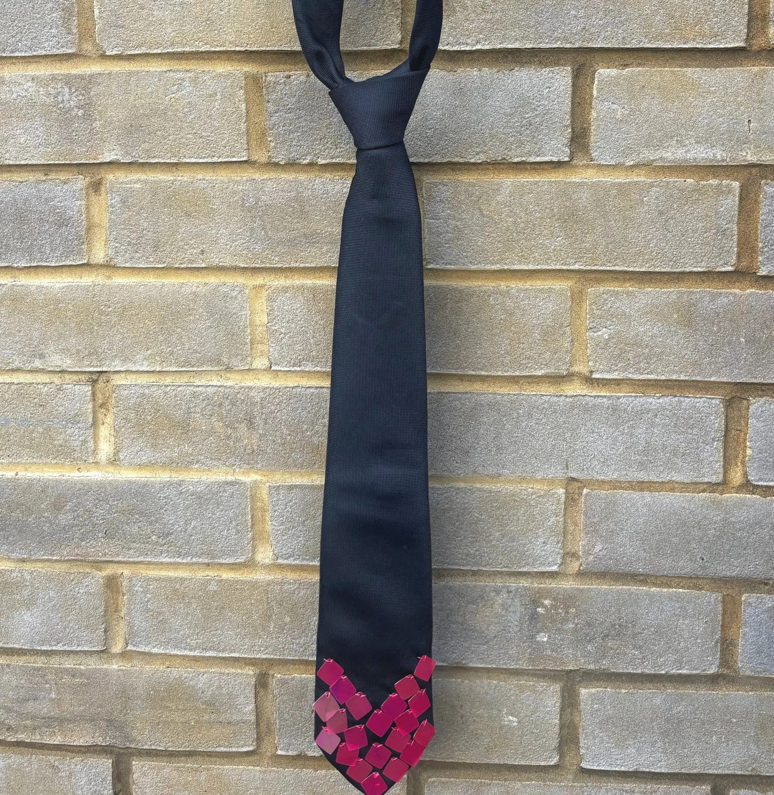 Black fabric handbag with pink decorative links hanging on a beige brick wall.