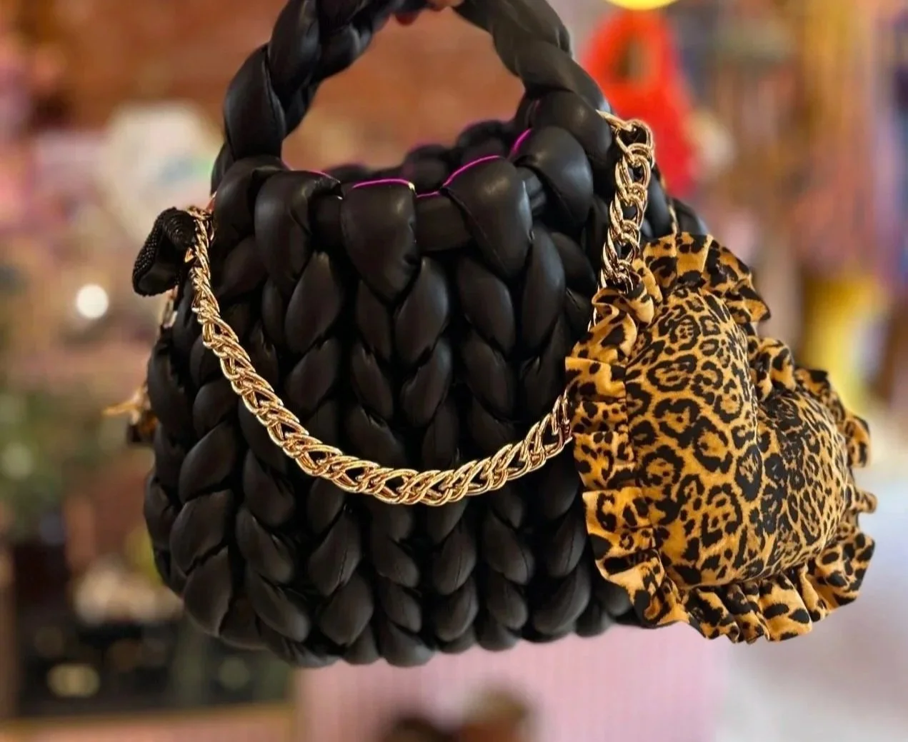 A woven black handbag with a gold chain strap and a leopard print scrunchie attached.