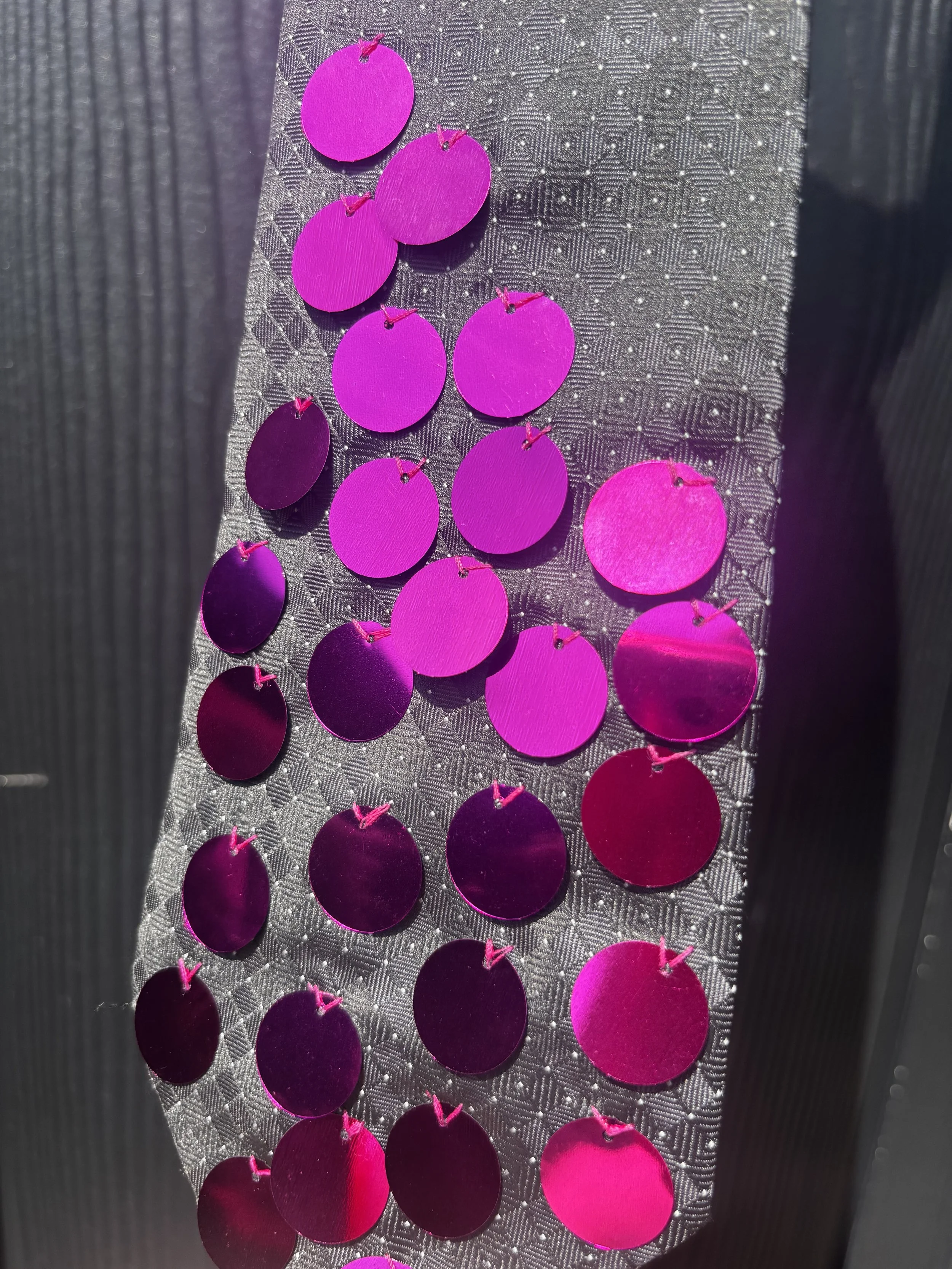 Close-up of bright pink circular sequins attached to a textured gray fabric surface.