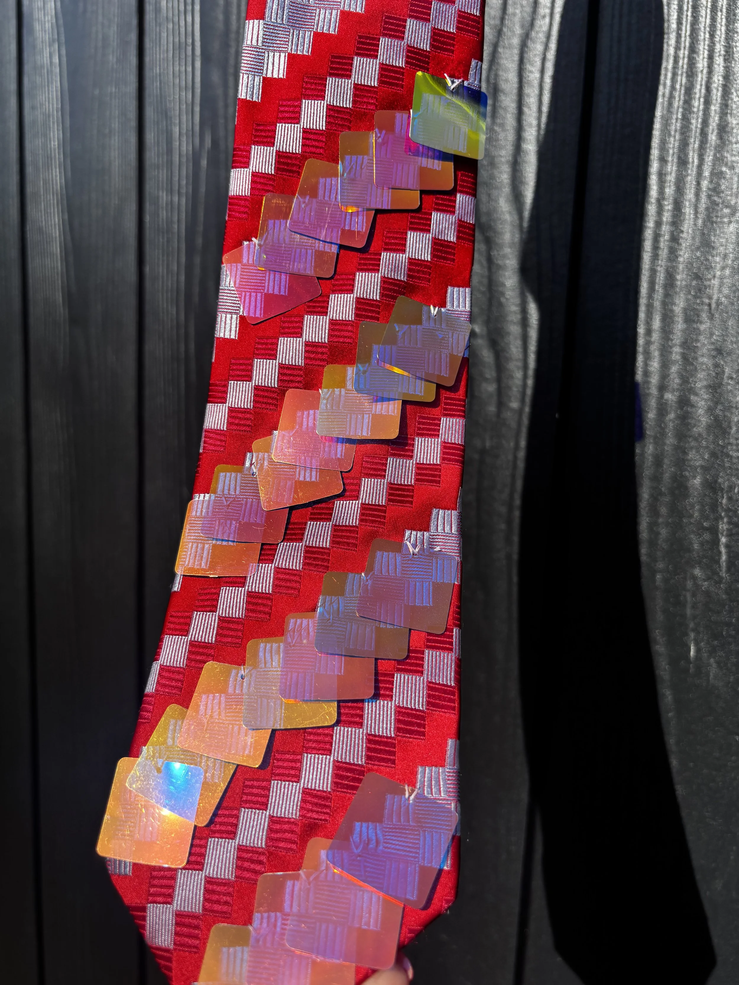 Close-up of a red and silver checkered ribbon with holographic rectangular stickers attached, set against a dark background.