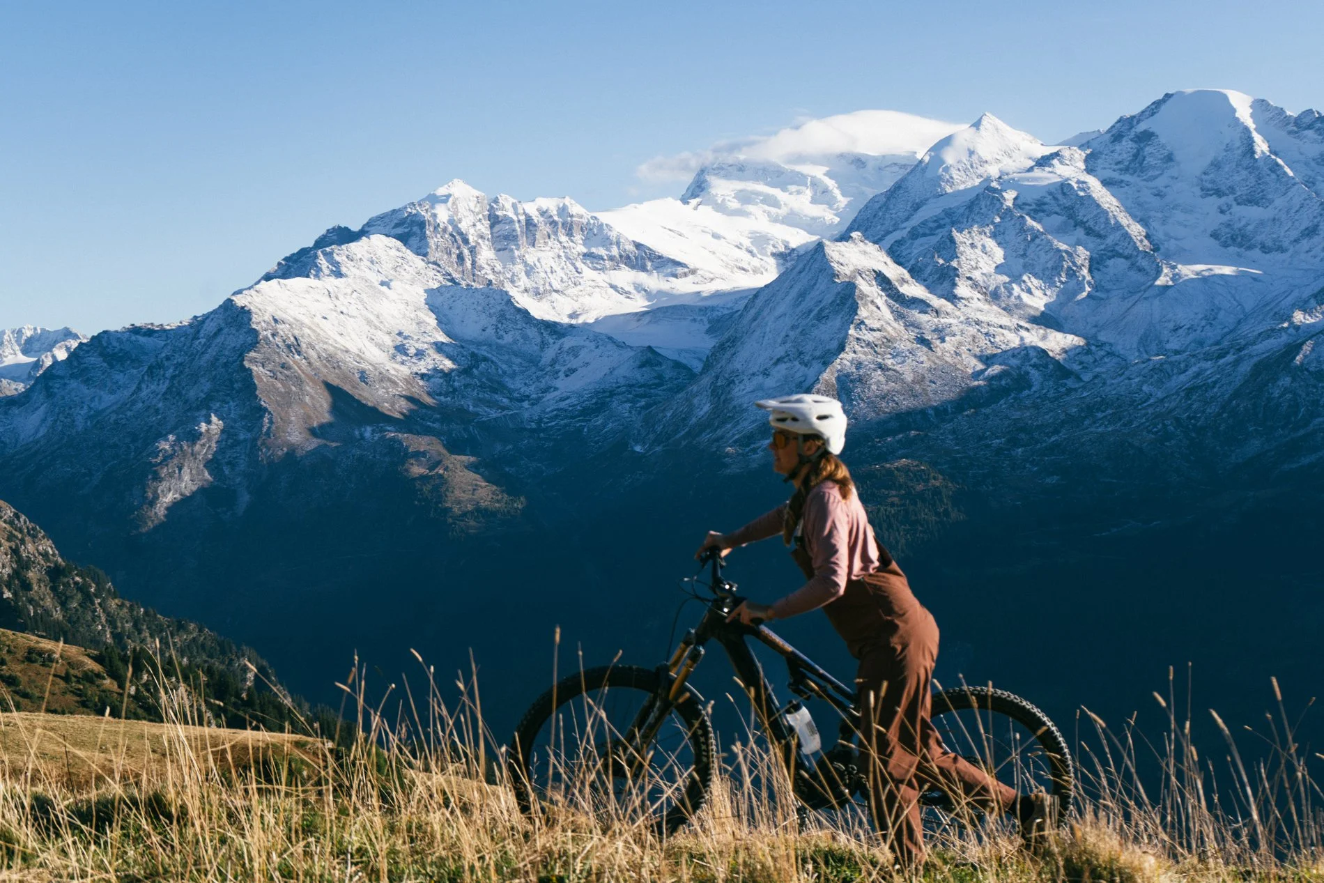 A person mountain biking through grassy fields with snow-capped mountains in the background.