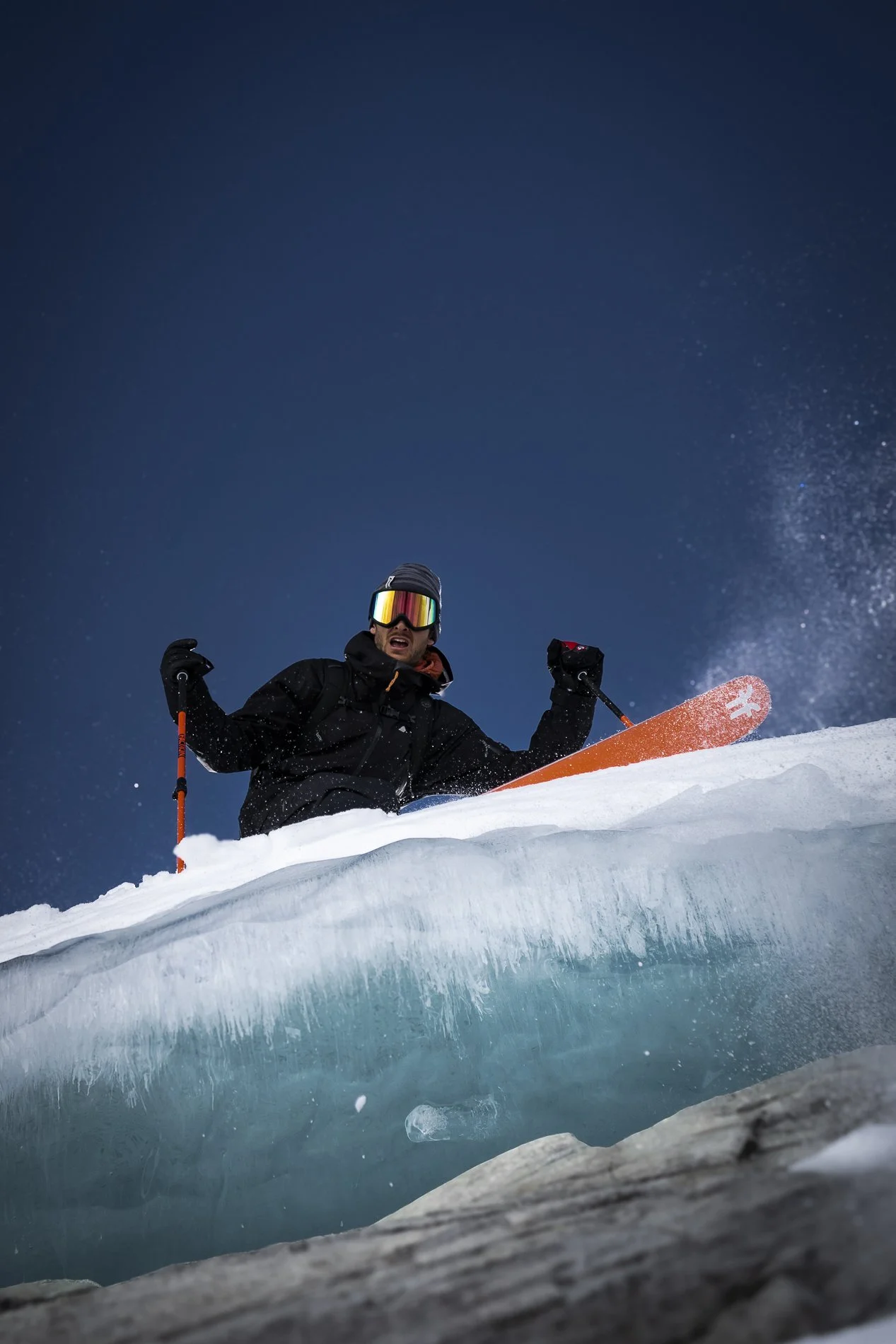 A person dressed in black snow gear and goggles skiing on an icy slope during night.