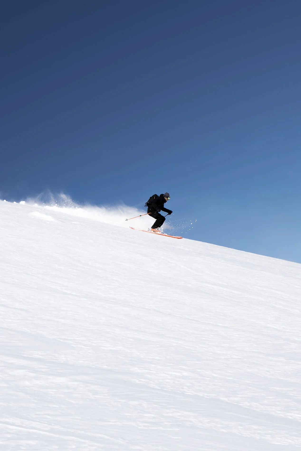 A person skiing down a snowy slope under a clear blue sky.