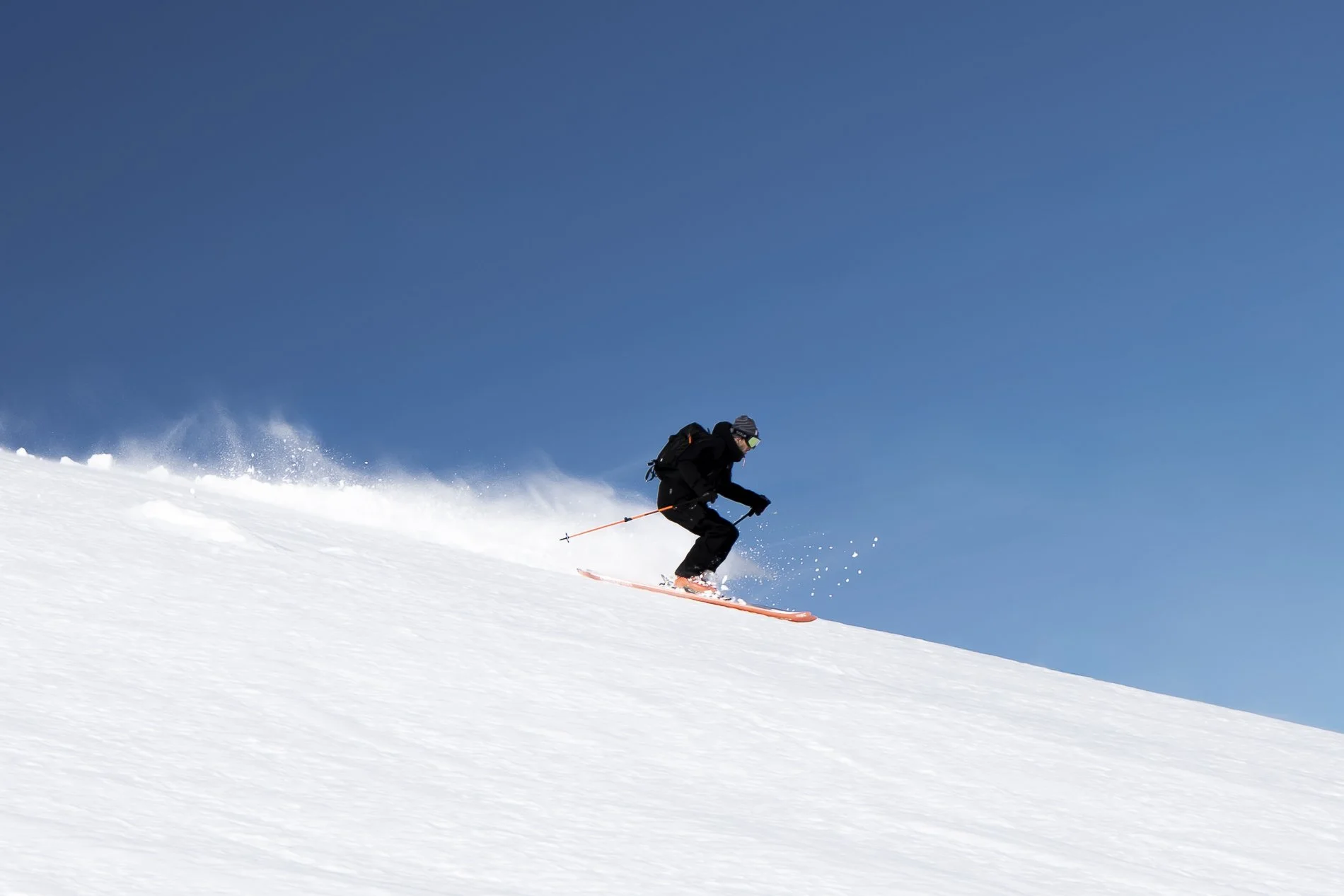 A person skiing down a snowy slope under a clear blue sky.