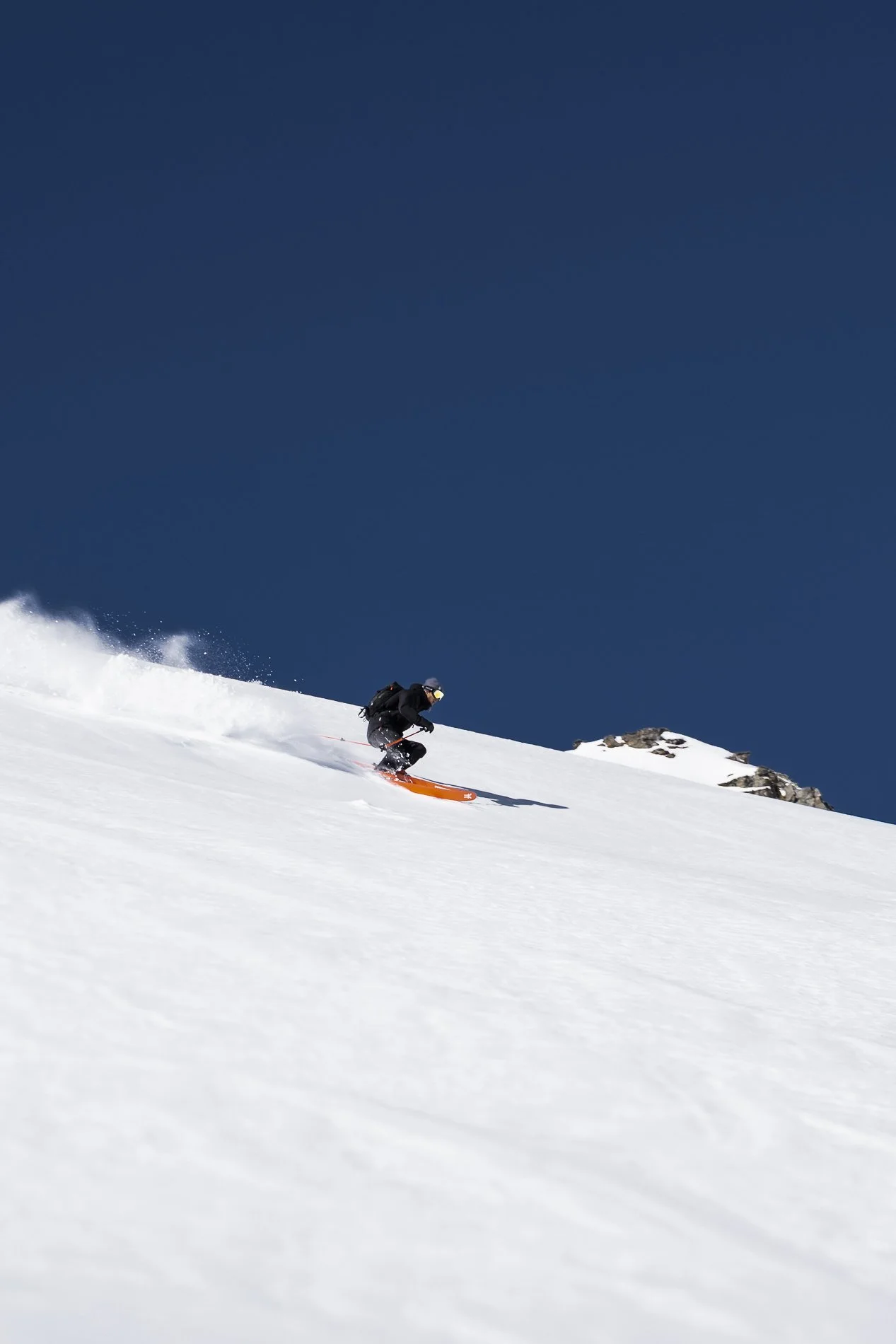 A skier skiing down a snowy slope in clear weather with a blue sky