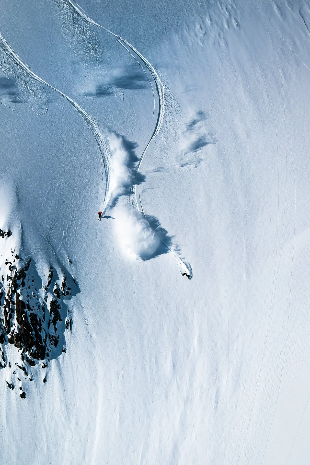 A skier descending a snow-covered mountain, creating a trail of snow.