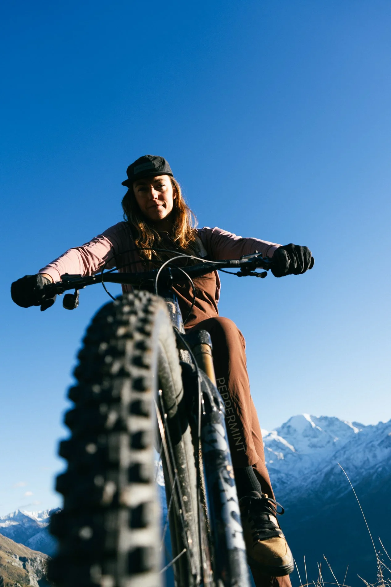 Person riding a mountain bike outdoors with snow-capped mountains in the background on a clear day.