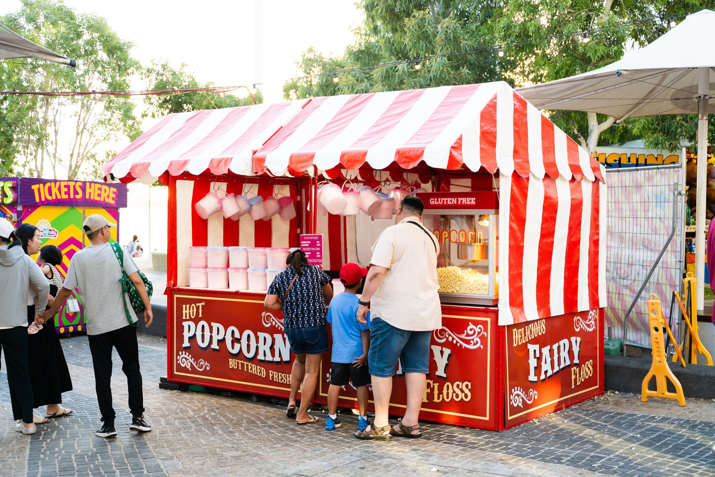 Popcorn stand at a fair with people in line, decorated in red and white stripes, selling buttered fresh popcorn.