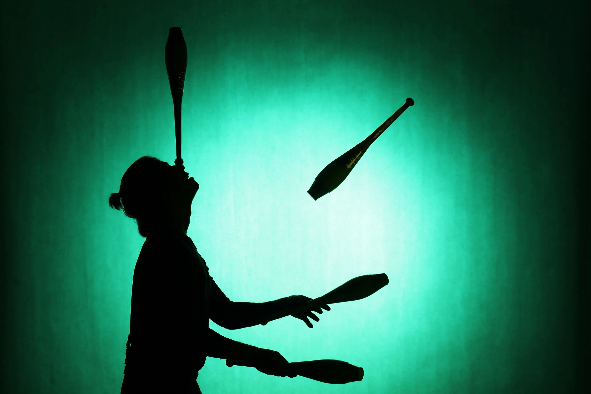 Silhouette of a person juggling machetes against a green background.