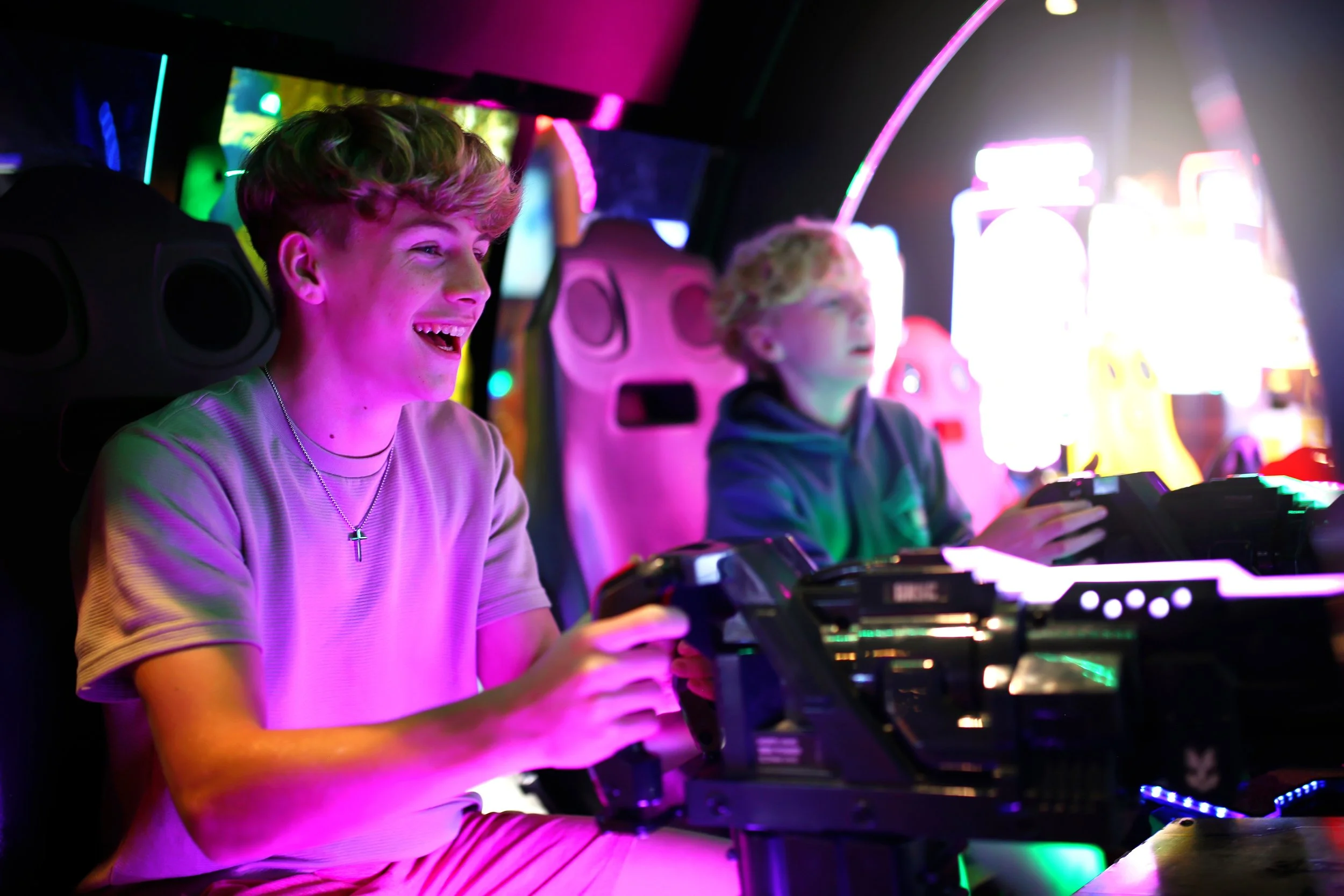 Two young men playing arcade dance game in an arcade with colorful neon lighting.