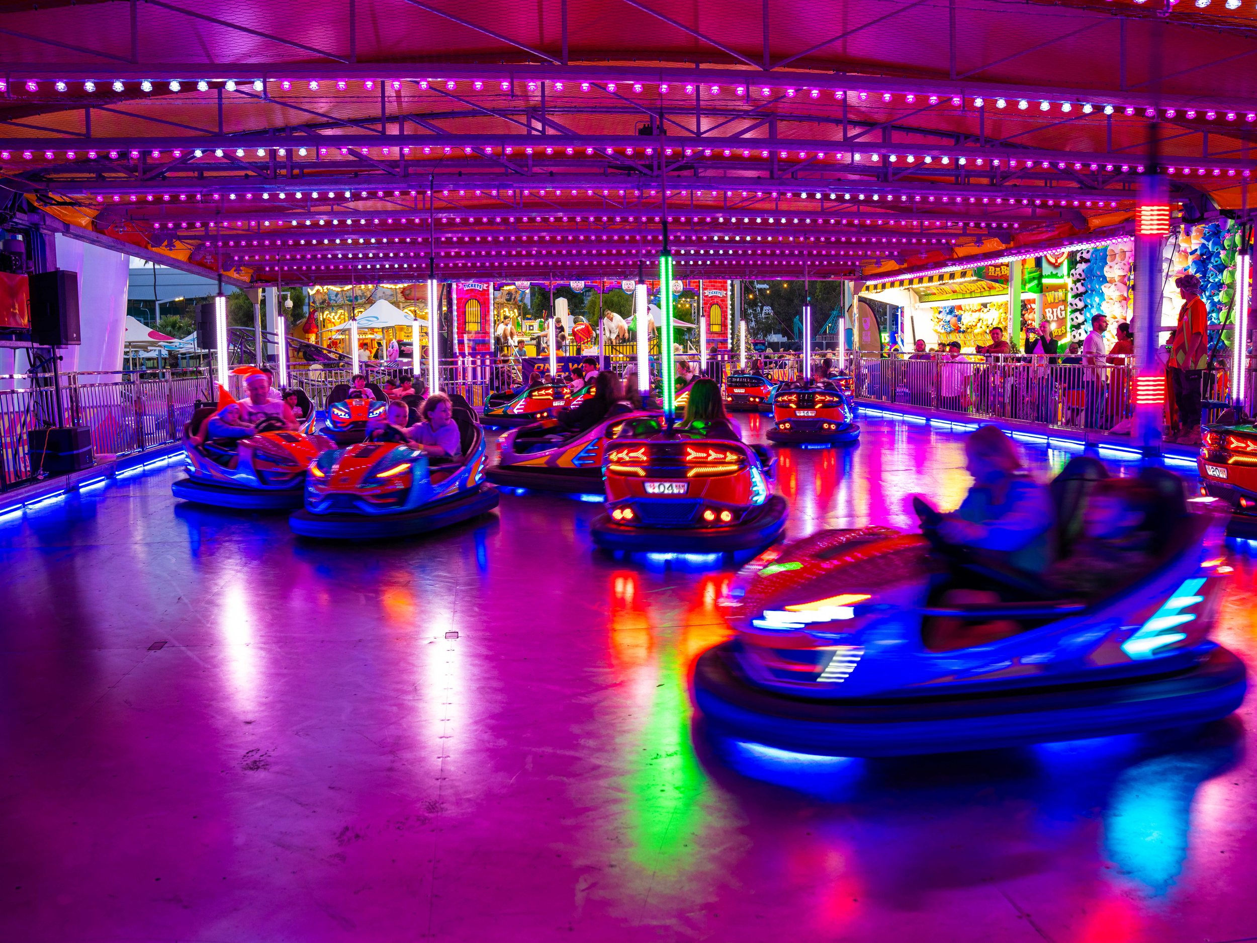 Colorful amusement park ride with spinning cars, surrounded by bright neon lights and a crowd of people.
