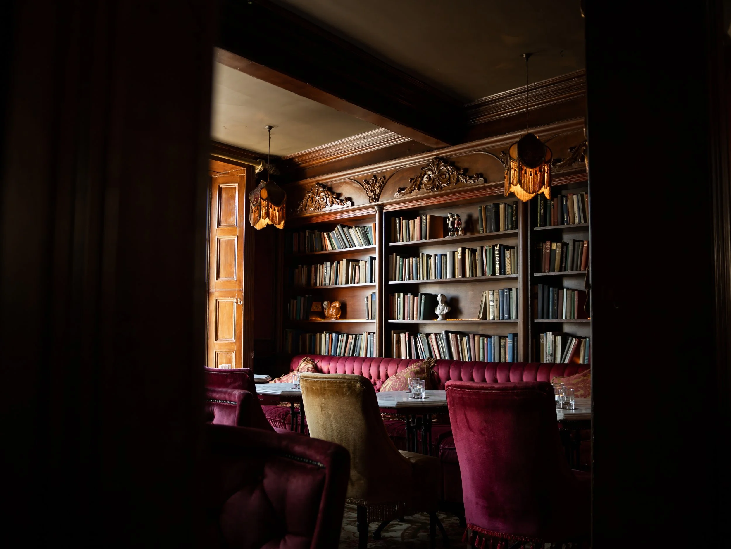 A cozy room with wooden bookshelves filled with books, ornate wooden trim, plush seating, and dim lighting from vintage lamps.