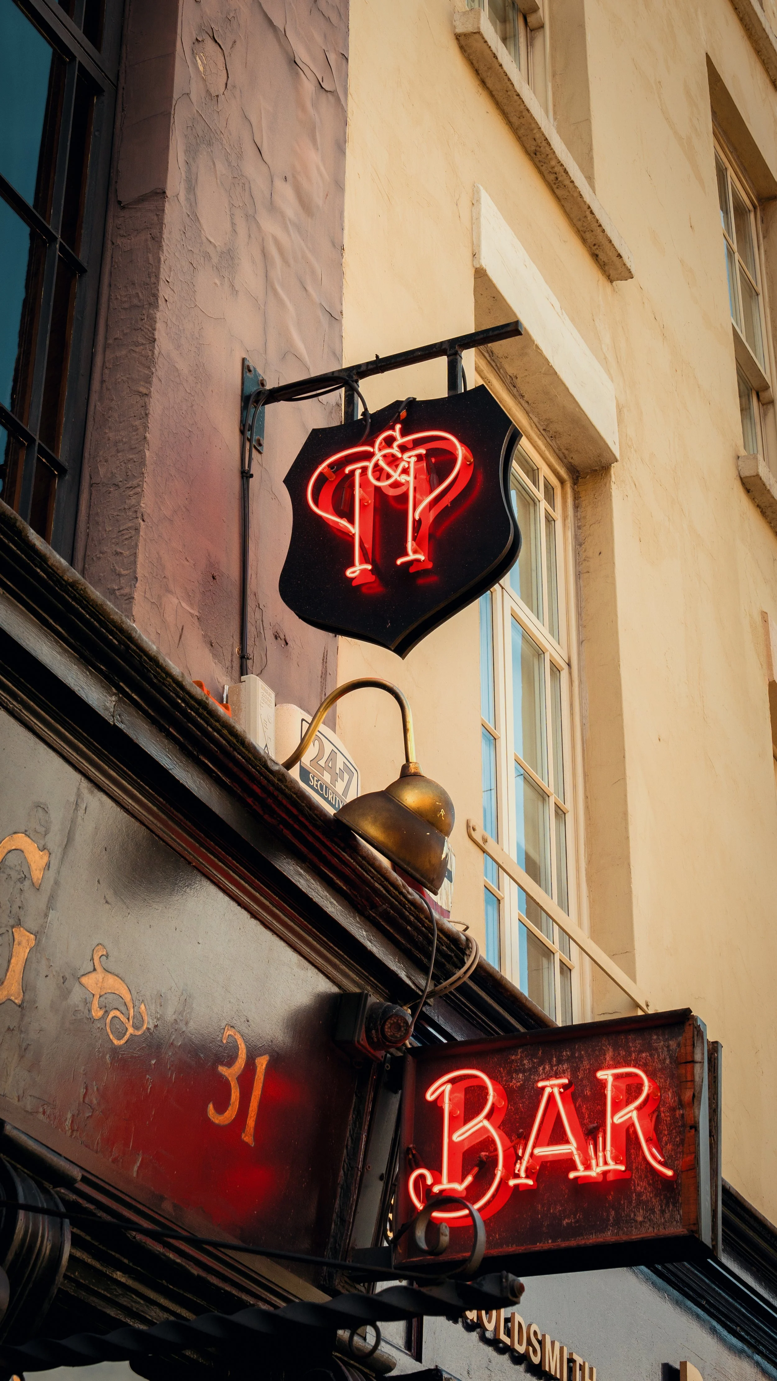 Neon bar sign with a martini glass and question mark, hanging on a building facade near windows.