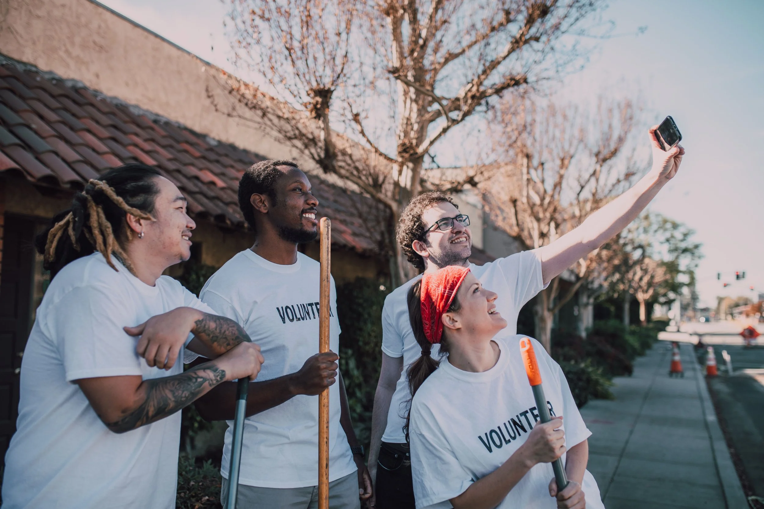 Group of four volunteers taking a selfie outdoors on a sunny day, standing in front of a house with trees in the background.