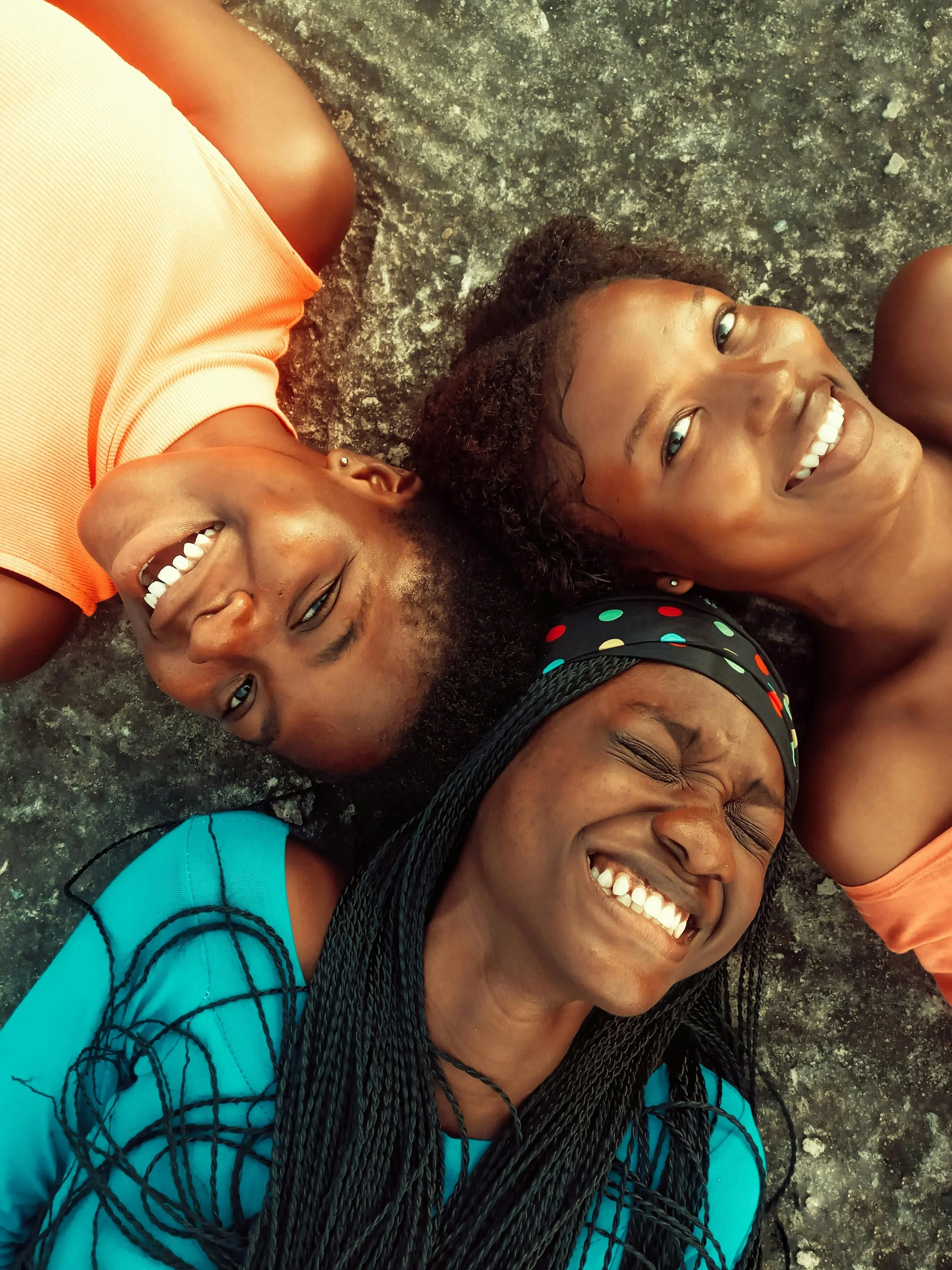 Four women lying on a rocky ground, smiling and enjoying a joyful moment in nature.