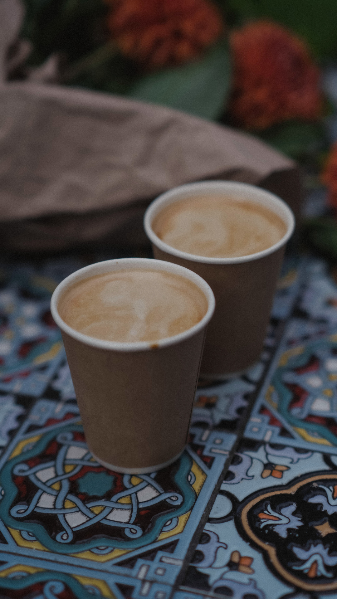 Deux tasses de café dans des gobelets en papier, posées sur une surface en mosaïque colorée avec des motifs complexes.