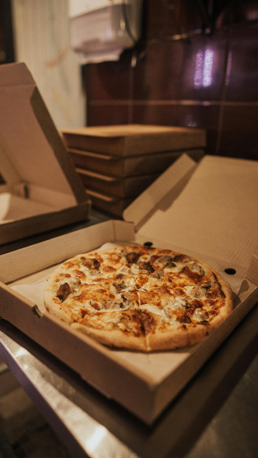 Une boîte à pizza ouverte contenant une pizza avec champignons et morceaux de viande sur une table dans un restaurant ou une pizzeria.