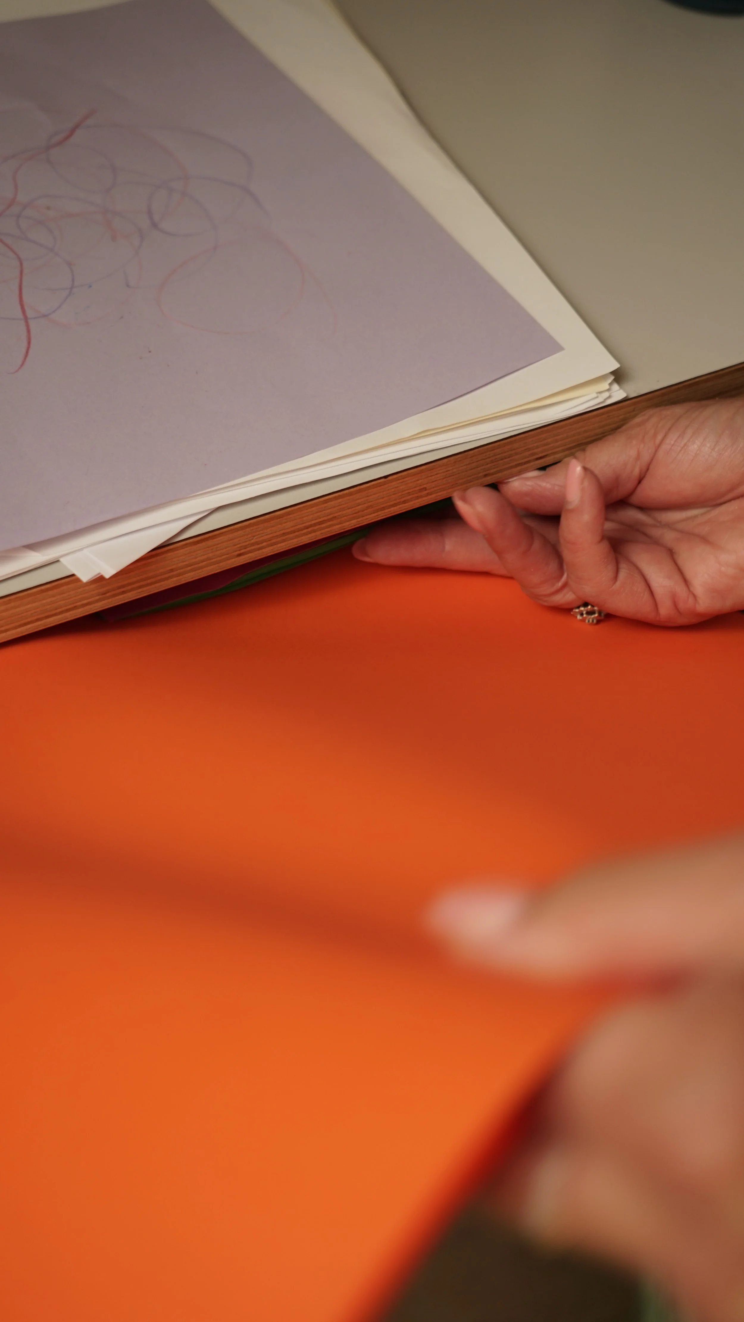Close-up van een hand dat een open boek vasthoudt met een tekening of krijt op een pagina. De achtergrond bevat een oranje oppervlak.