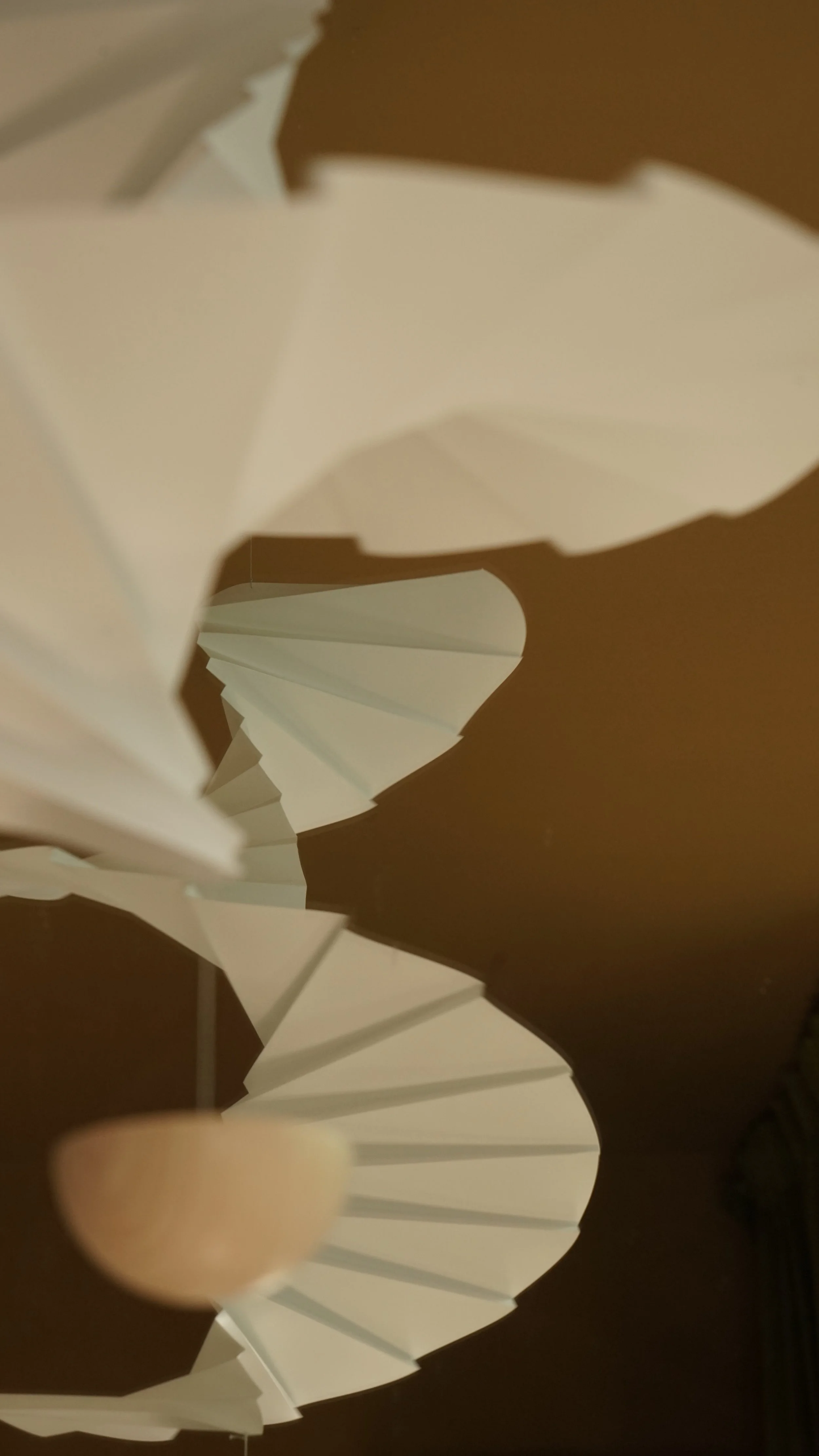 Een witte papieren lampenkap met een spiralenvorm, gevouwen in een zigzag patroon, bevestigd aan een staander.
