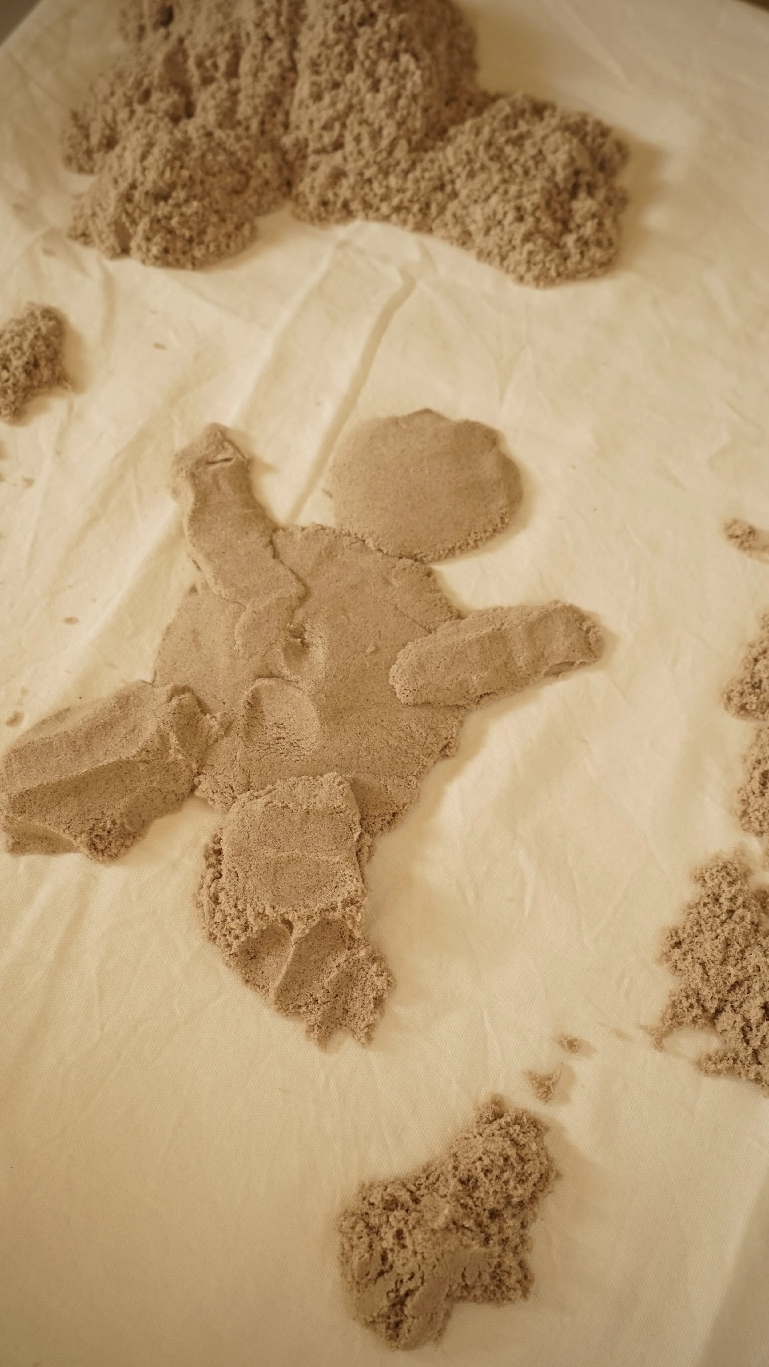 Op een wit vel liggen verschillende vormen van klei in grijze en beige tinten, deels in blokken, deels in losse stukjes.