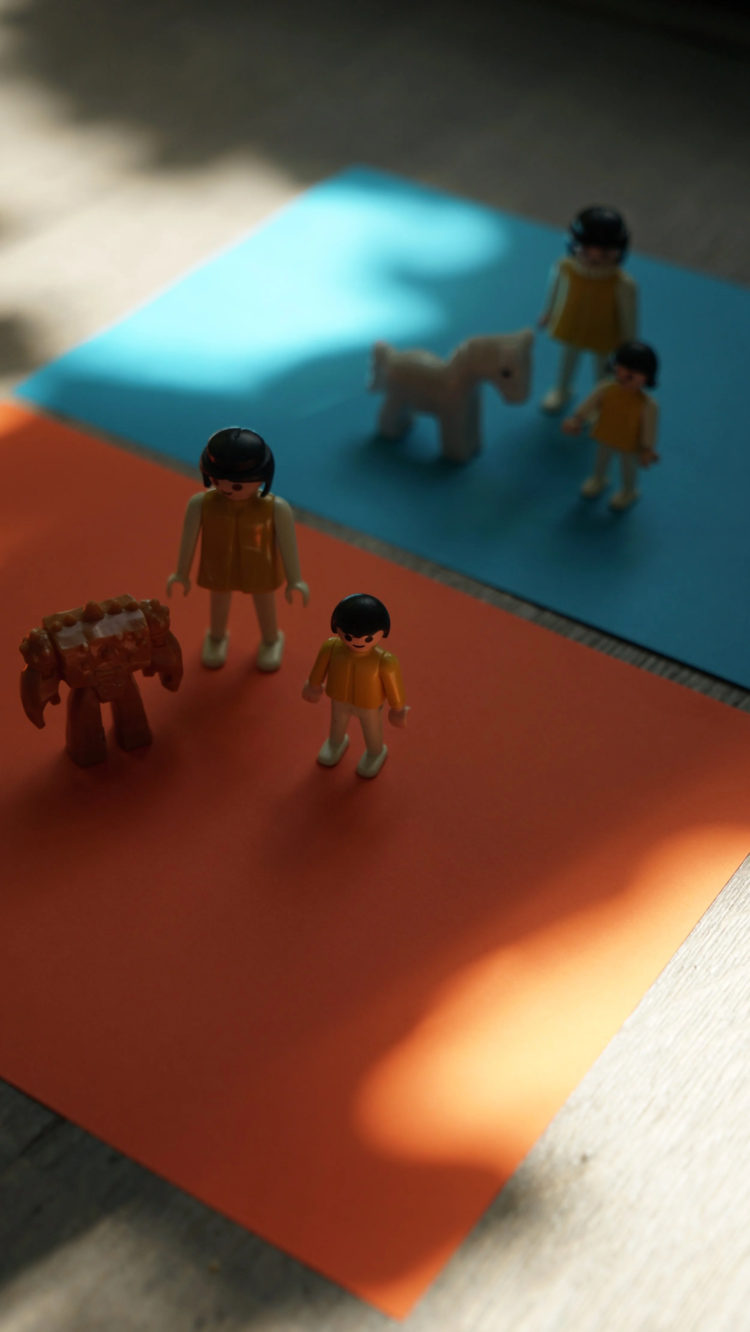Miniatuurfiguren op een kleurenbord met een witte eenhoorn en twee meisjes, een blauwe en een oranje achtergrond.