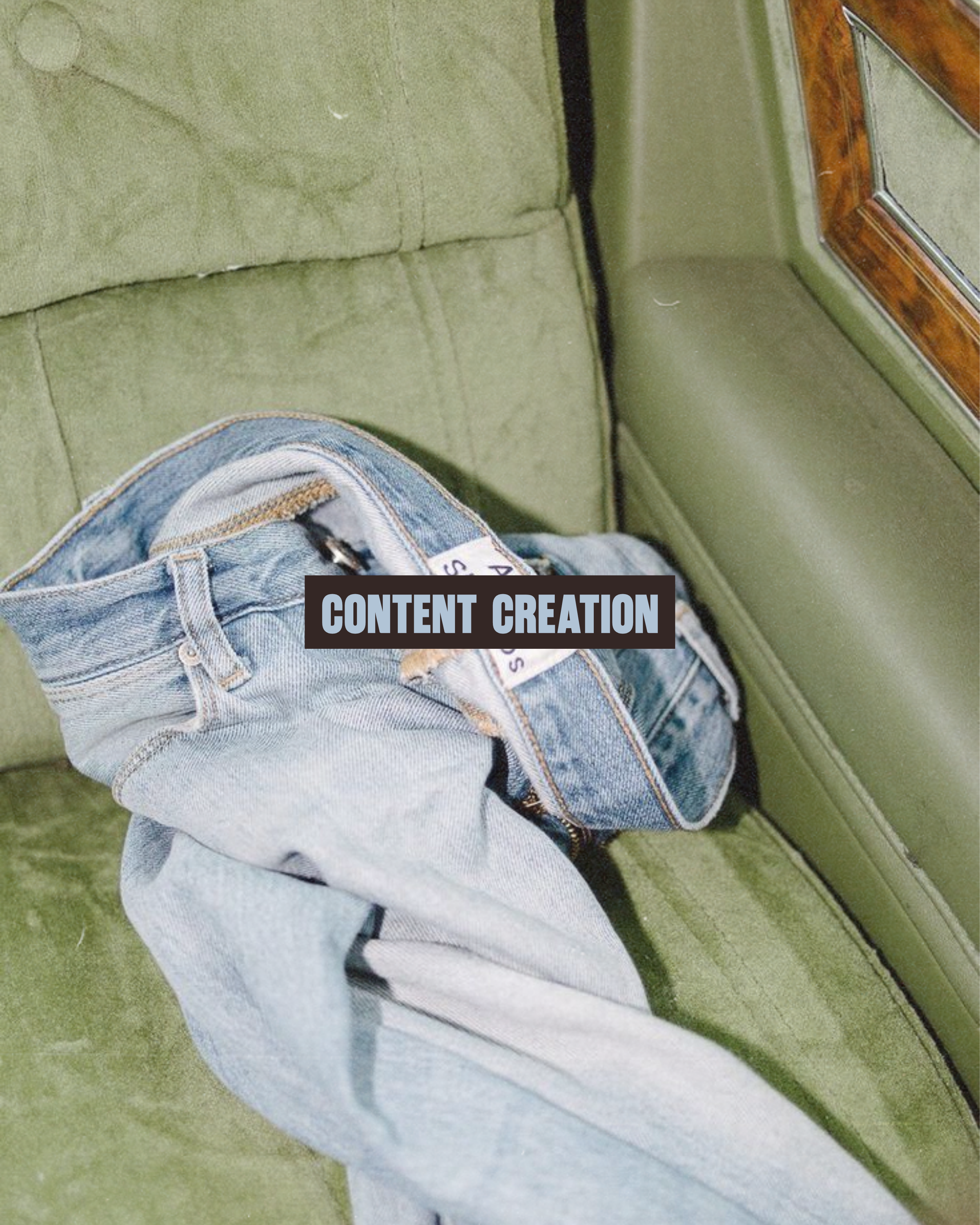Close-up of a green vintage sofa, part of a hardwood table, and a person wearing ripped blue jeans with a black strap visible.