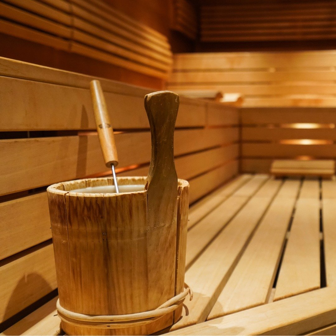 A wooden bucket with a ladle and a paddle inside, placed inside a wood-paneled sauna.