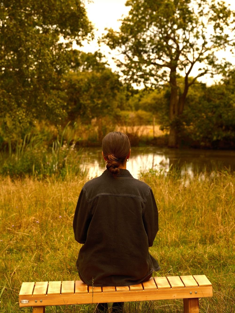 Woman sat on a wooden bench looking out over a lake