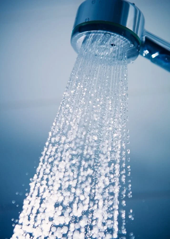 Close-up of a showerhead releasing water droplets downward, with a blue-toned background.
